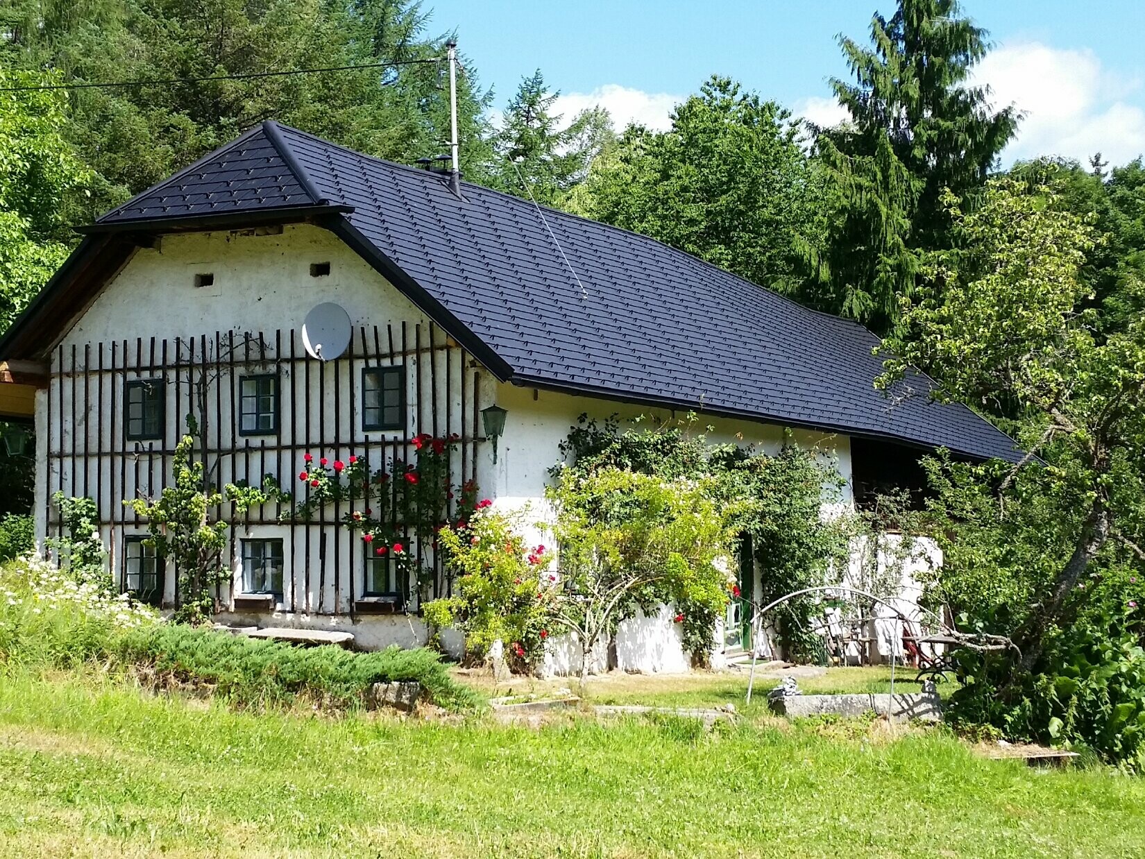 This picture shows an old farmhouse after the roof has been renovated. The roof of the so-called meadow house is covered with PREFA roof shingles P.10 black. 