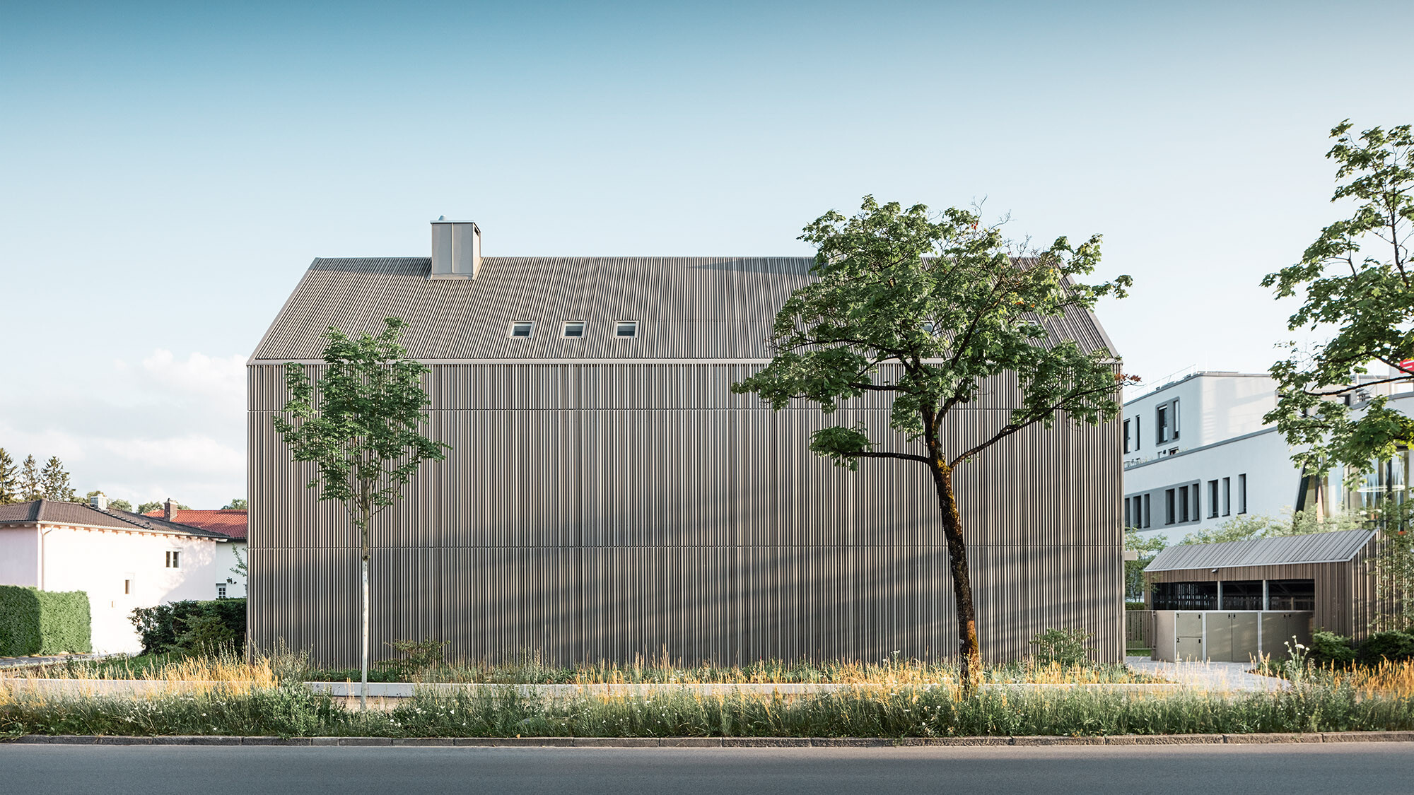 Frontal view of the calm, closed side of the building from the other side of the street with trees and green areas before it. 