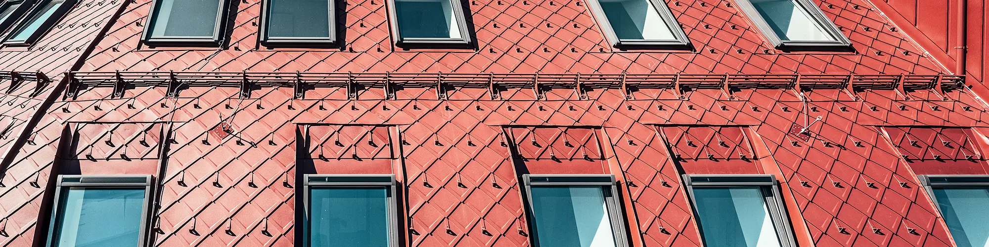 Close-up of the striking roofscape made of oxide red aluminium rhomboid tiles.