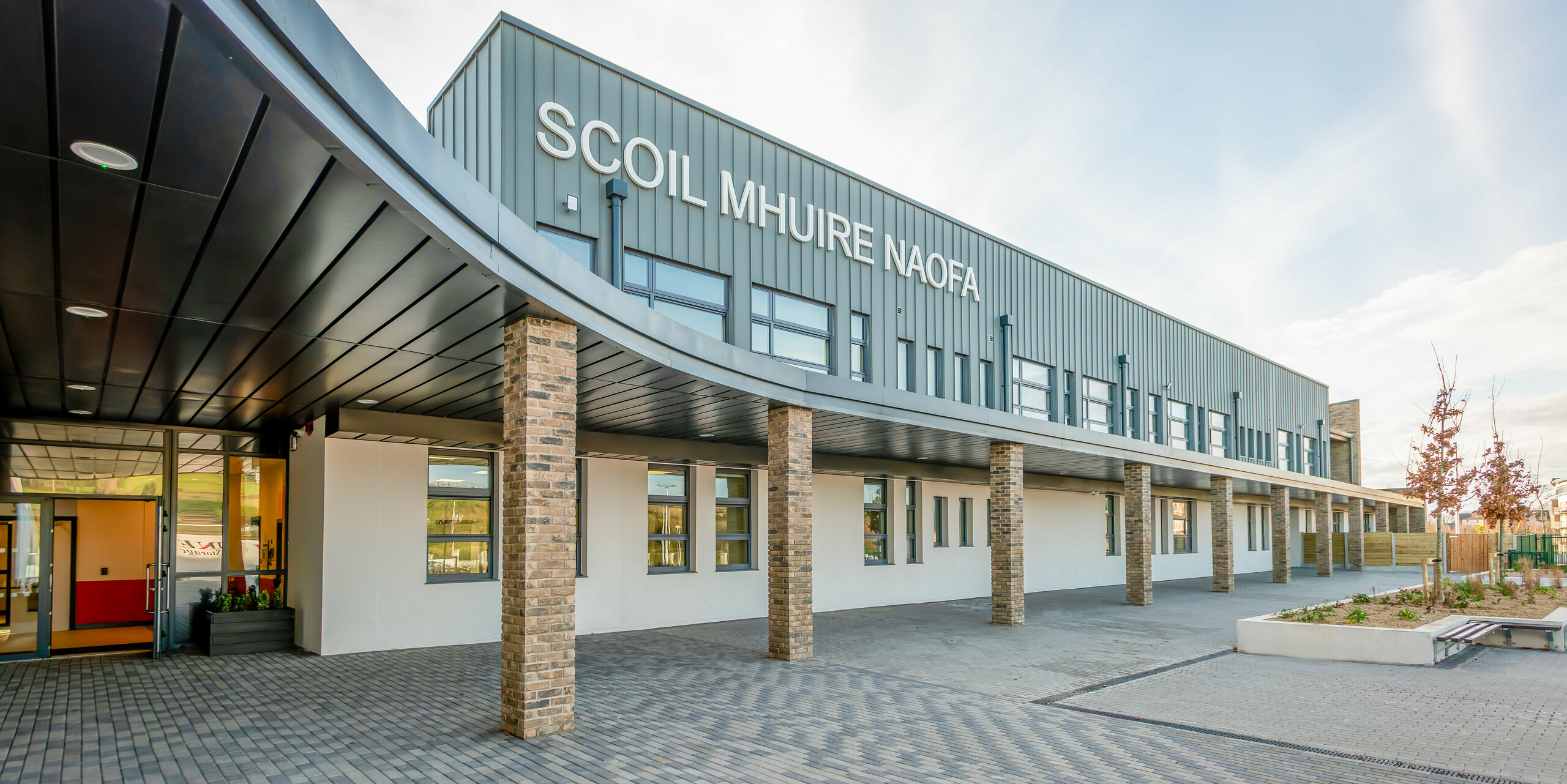 Detailed view of the main entrance of the new Scoil Mhuire Naofa in Carrigtwohill, Ireland. The modern façade made of PREFALZ aluminium in P.10 light grey combined with brick columns gives the building a timeless elegance. The covered area and the generous windows along the entire side of the building create a welcoming atmosphere for students and visitors.