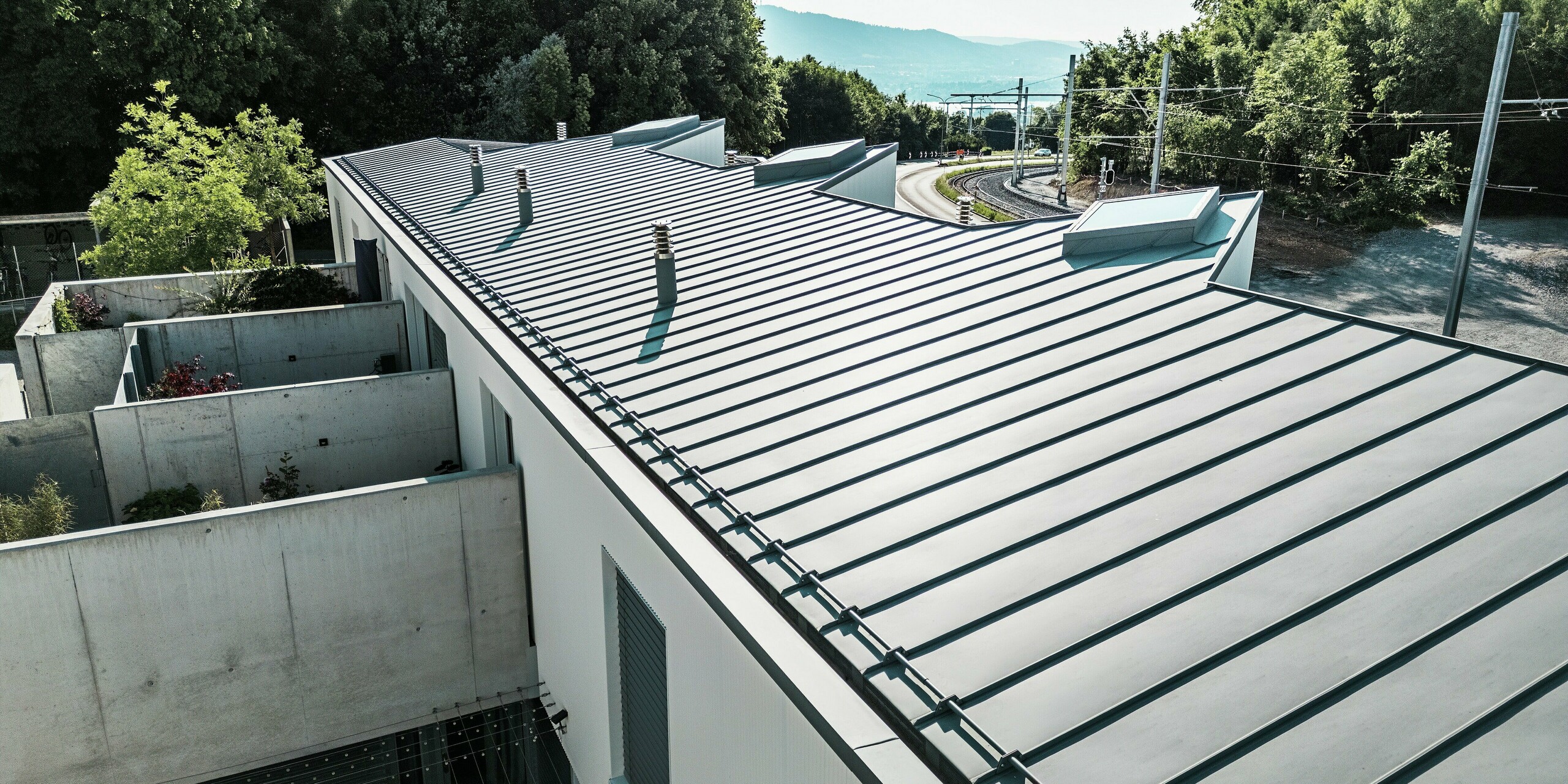 Langgezogene Dachansicht eines Tiny Homes Wohnkomplexes in Zollikerberg mit hochwertigem PREFALZ Stehfalzdach in Patinagrau. Das witterungsbeständige PREFA Aluminiumdach passt sich harmonisch der modernen Architektur und der naturnahen Umgebung an. Die klare Linienführung, integrierten Dachaufbauten und die nachhaltige Materialwahl machen dieses Dach zur langlebigen Premiumlösung.