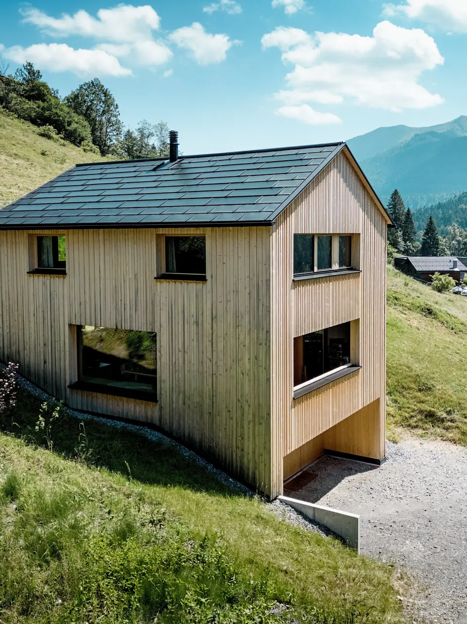Hoch über dem Tal steht Haus Immi wie ein klarer Holzmonolith im sonnigen Berghang von Ebnit. Die reduzierte Weißtannenfassade und das schwarze PREFA Solardach setzen einen kraftvollen Kontrast zur weiten Alpenlandschaft. Integrierte Solardachplatten und Dachplatten R.16 in P.10 Schwarz liefern Solarstrom, trotzen alpinem Wetter und sichern ein langlebiges, harmonisches Dachbild.