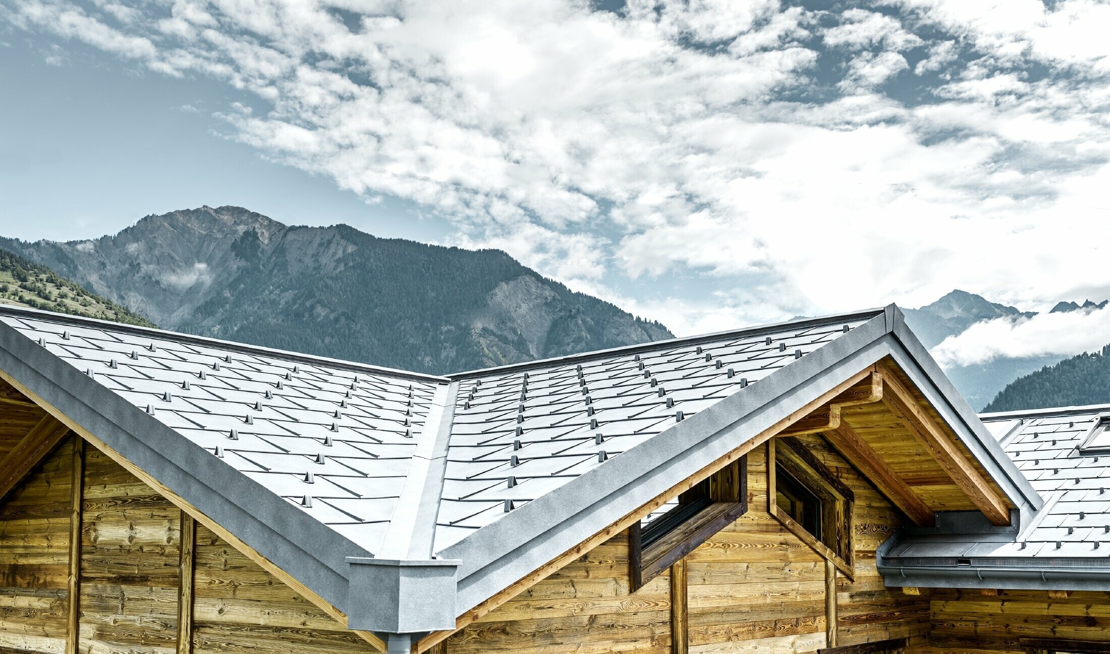 Roof of a rustic cottage in Switzerland with wooden façade and a PREFA aluminium roof. The R.16 roof tile in stone grey was installed. The angled roof and valley are clearly distinguishable.