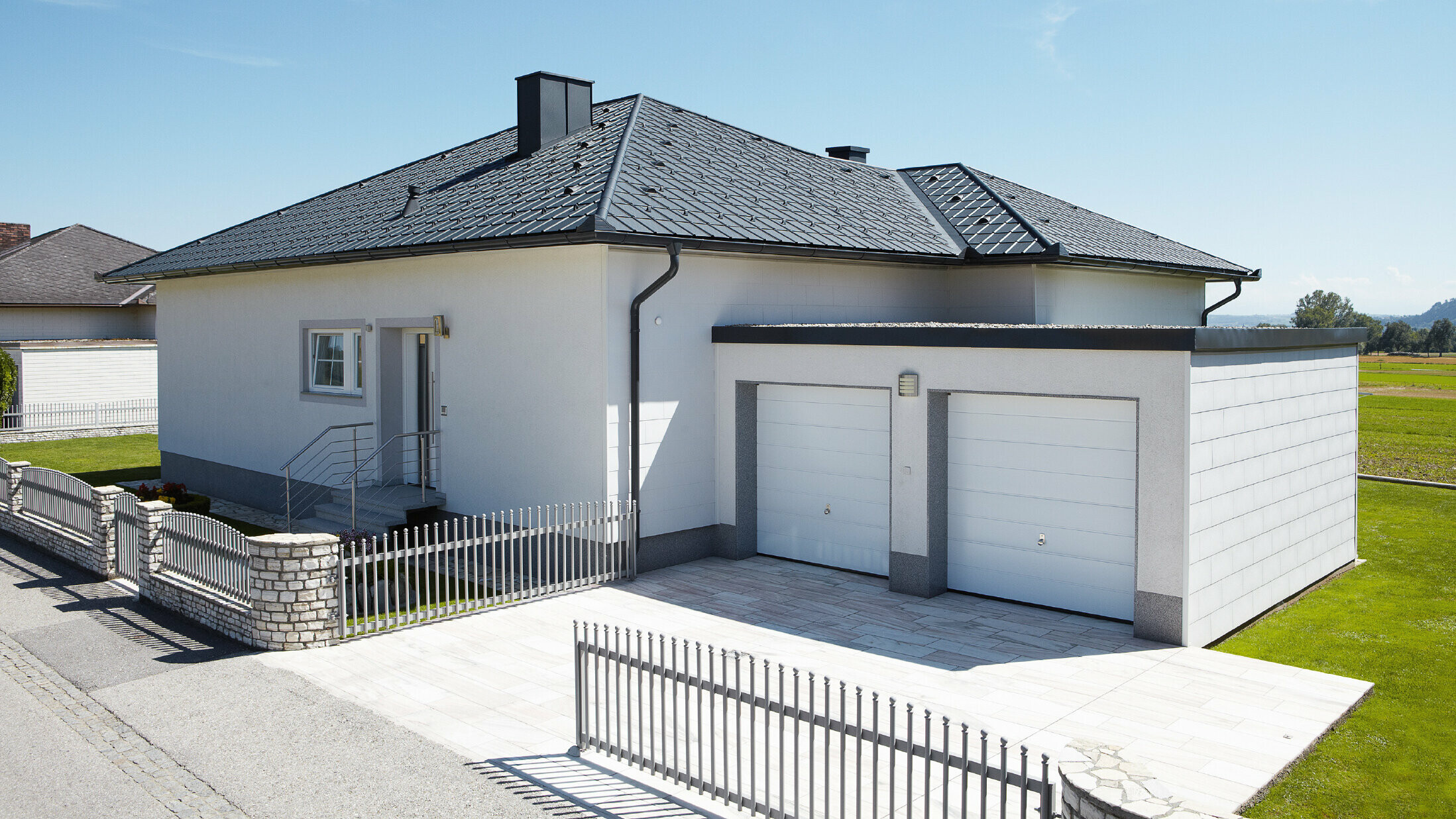 The newly built bungalow with a tent roof was covered with PREFA roof tiles in P.10 anthracite. A double garage was built to the right of it, photographed from the street.