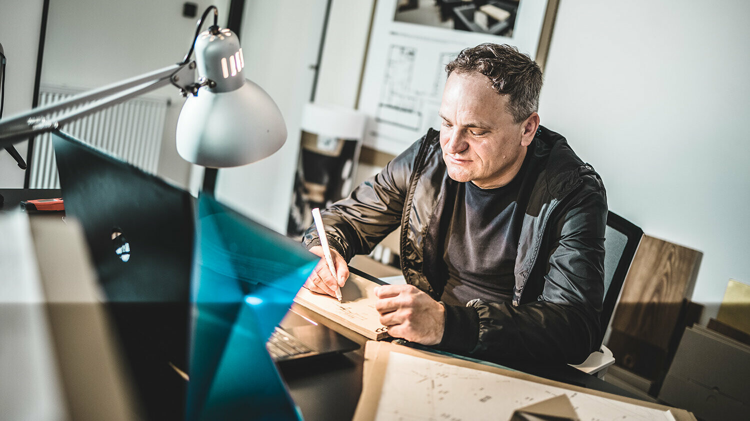 Portrait of Daniel Zerzán at his office, his view is directed towards the notepad lying before him and he is writing on it.