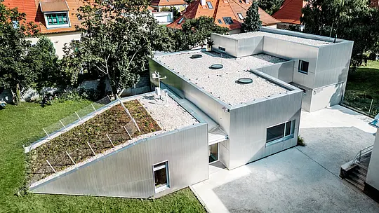 Aus der Vogelperspektive begeistert das Envirocenter Nitra mit seiner außergewöhnlichen Architektur und der silbern schimmernden PREFA Aluminiumfassade aus Strangpressprofil Welle in Naturblank. Die langlebigen, witterungsbeständigen Aluminiumprofile verbinden die unterschiedlich hohen Baukörper zu einer harmonischen Einheit. Ein begrüntes Schrägdach, helle Flachdächer und die umliegenden historischen Gebäude bilden einen spannenden architektonischen Kontrast.