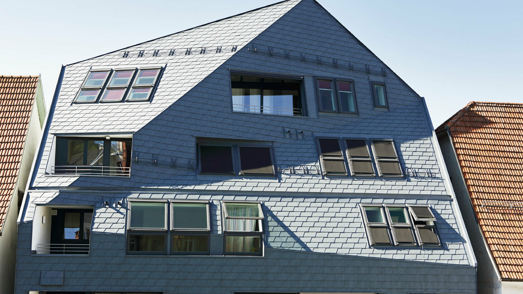 Gallery house with folded façade surface, clad with the PREFA roof and façade shingles in P.10 stone grey with many windows