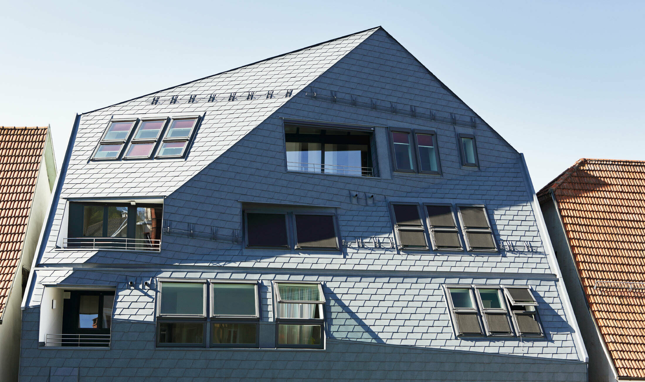 Gallery house with folded façade surface, clad with the PREFA roof and façade shingles in P.10 stone grey with many windows