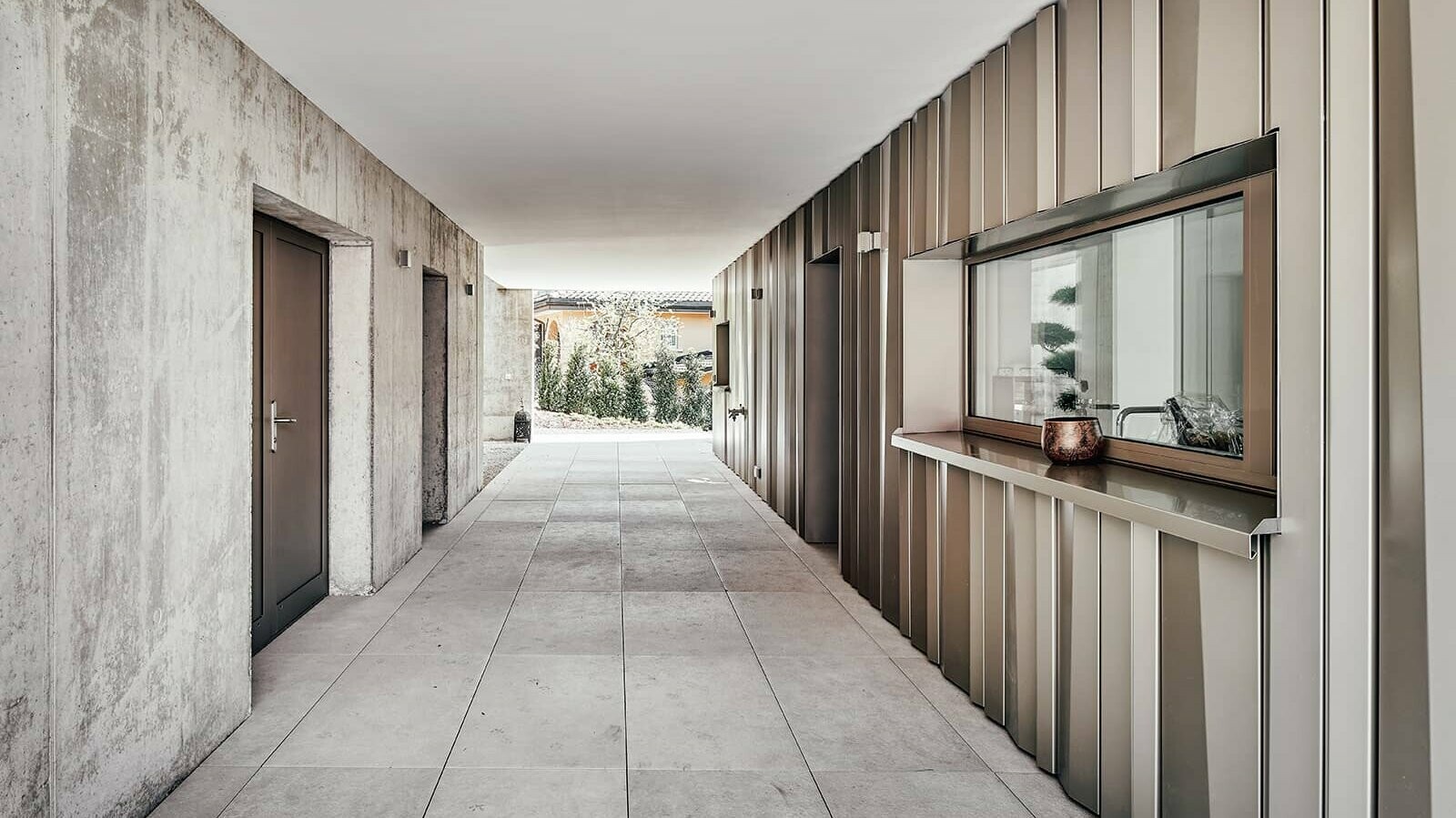 Exterior view of the entrance area of the detached house. On the left, the façade has a concrete look. On the right, the façade is covered with PREFA metal sheets in bronze.