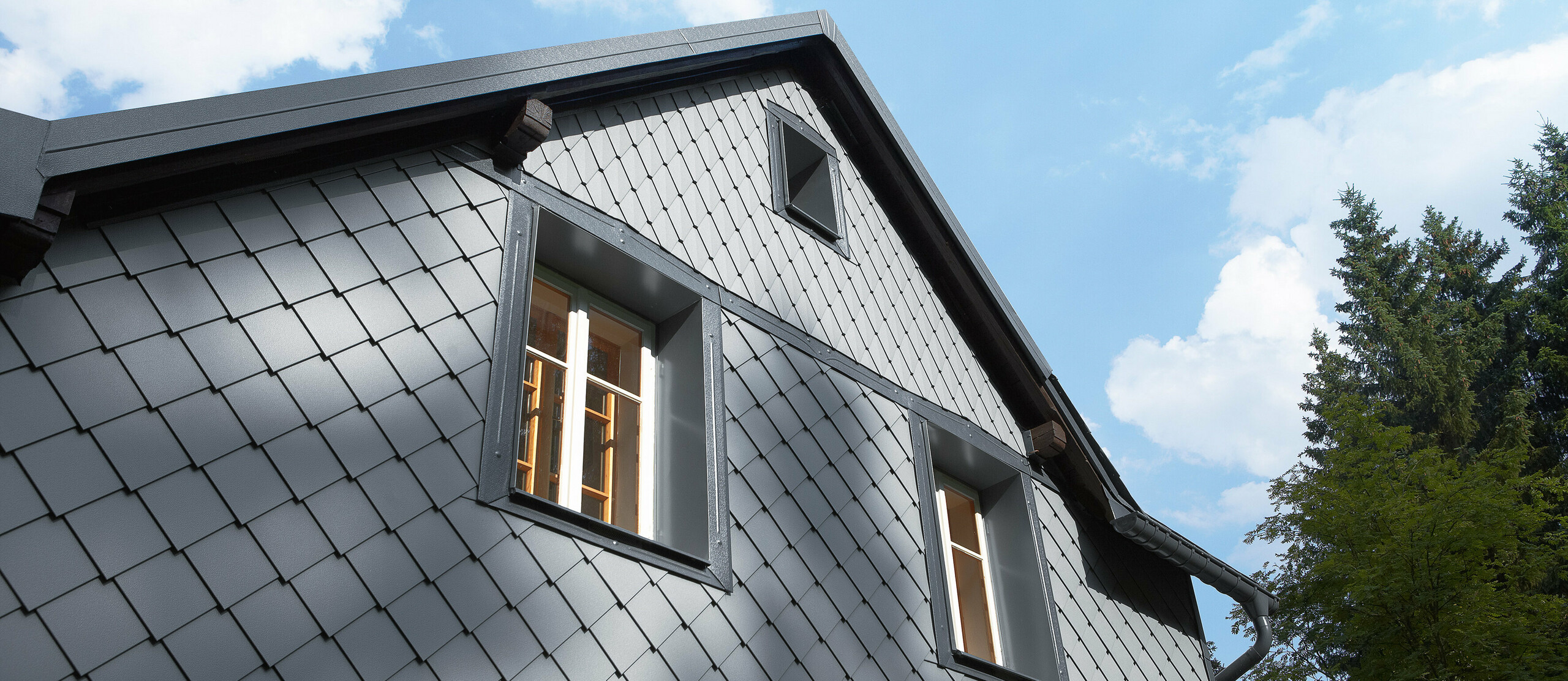 The side of a building that faces the direction of the prevailing weather clad with PREFA’s rhomboid façade tile 20 × 20 and small-format rhomboid tile on the façade