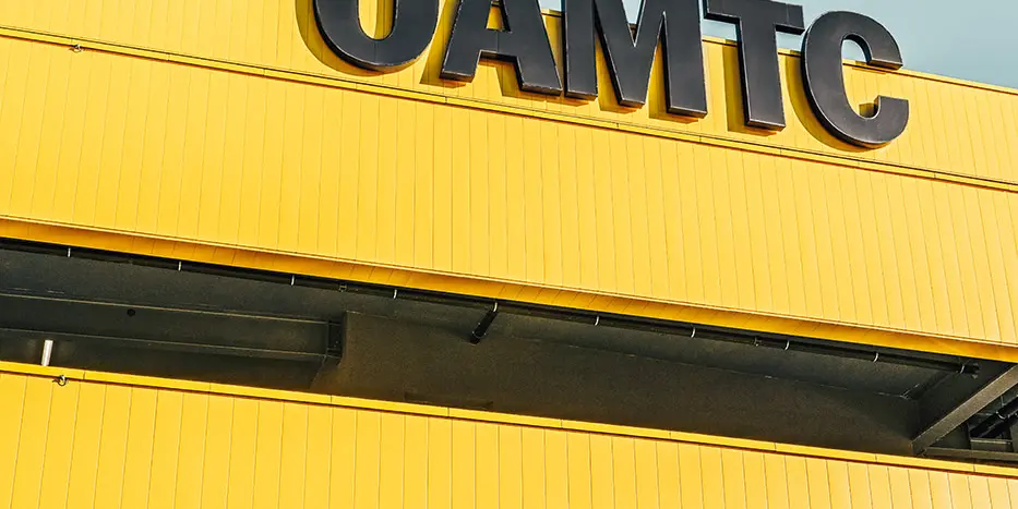 Close-up of the ÖAMTC Logo. The façade is covered in PREFA Sidinds in the bespoke colour rapeseed yellow and slate grey.