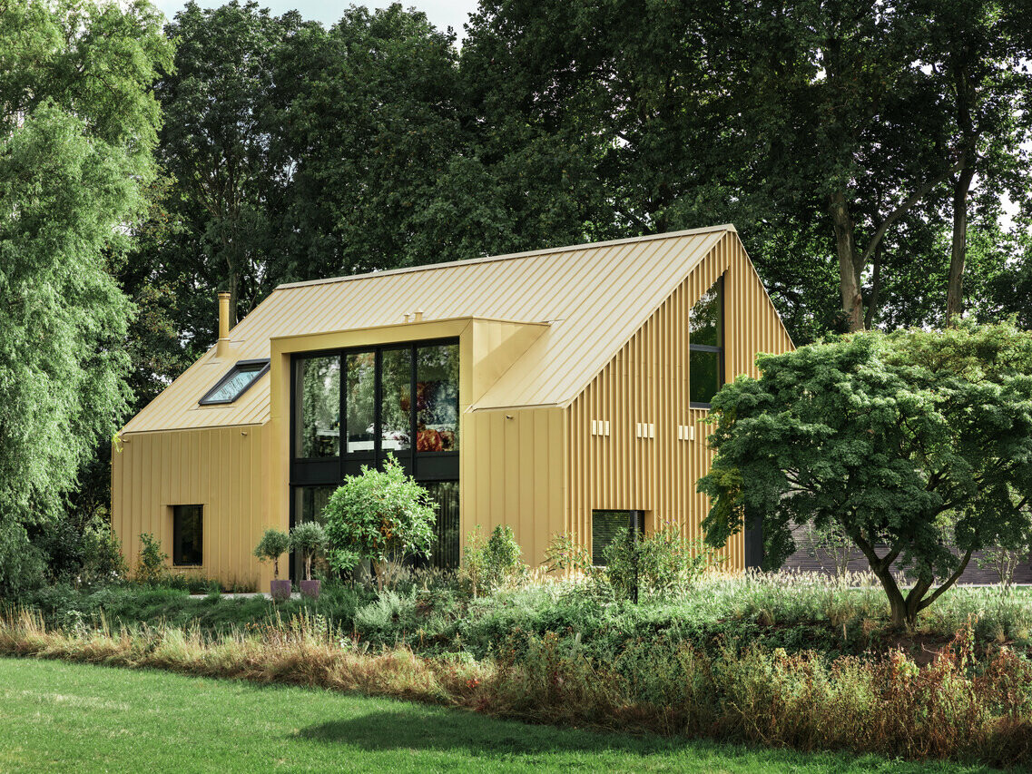 Side view of the PREFA-covered detached house in Elst (NL). Bushes and trees surround the building.