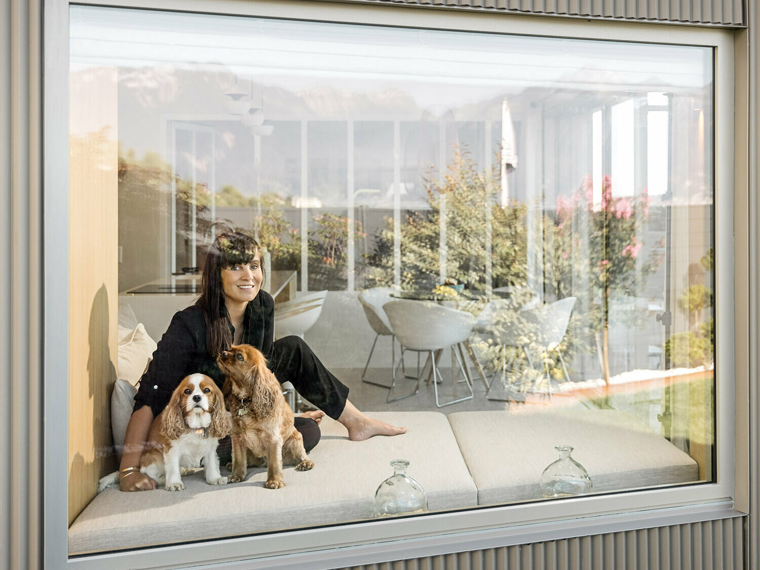 Portrait of Sophie Morard sitting behind the window with her two dogs in her lake house.