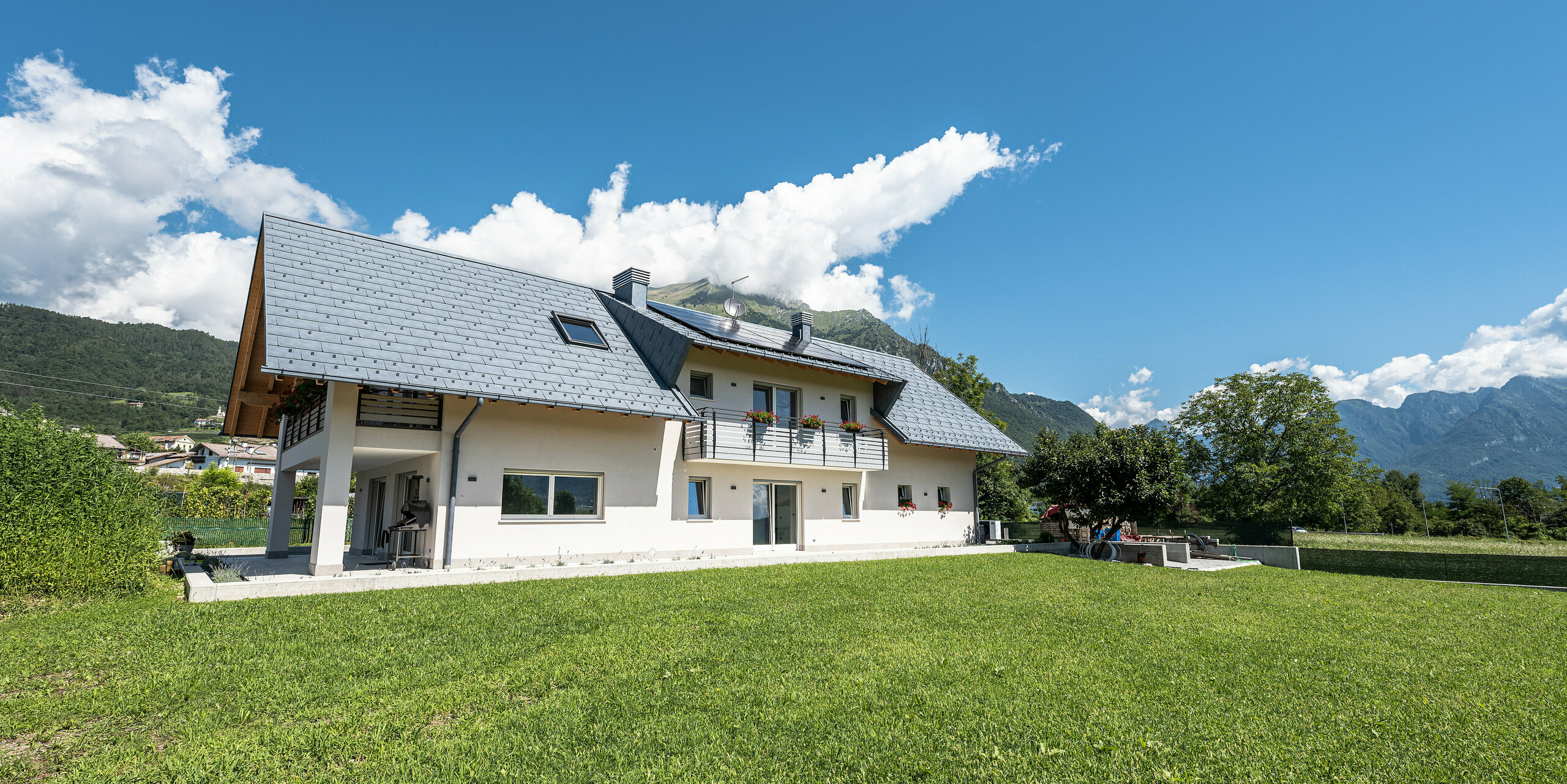 Idyllisch gelegenes Einfamilienhaus in Bellun, Italien, mit einem robusten Aluminiumdach aus PREFA R.16 Dachpaneelen in P.10 anthrazit. Mit traditionellem weißen Putz und modernem Aluminiumdach fügt sich das Anwesen harmonisch in die malerische Landschaft mit atemberaubendem Blick auf die umliegenden Berge ein.