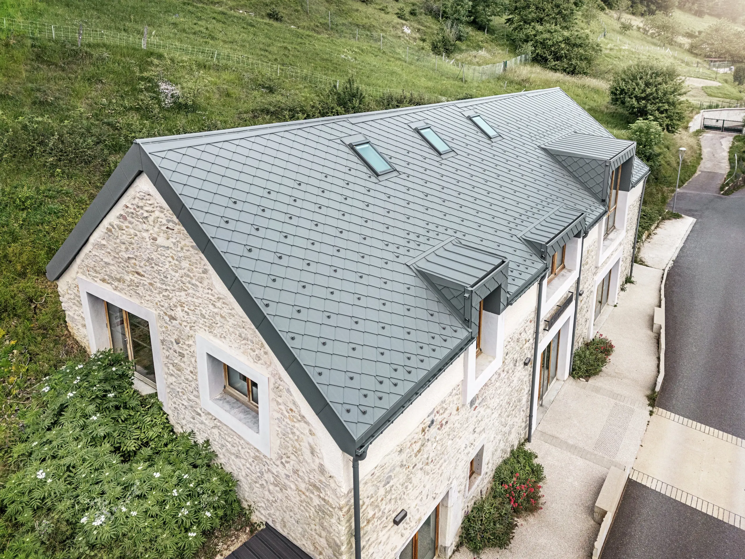 View of the roof of the restored barn ‘La Grange à Gaby’ in Engins, France. The modern PREFA aluminium roof with 29 × 29 rhombus tiles blends harmoniously into the historic stone building and provides long-lasting protection against the weather.
