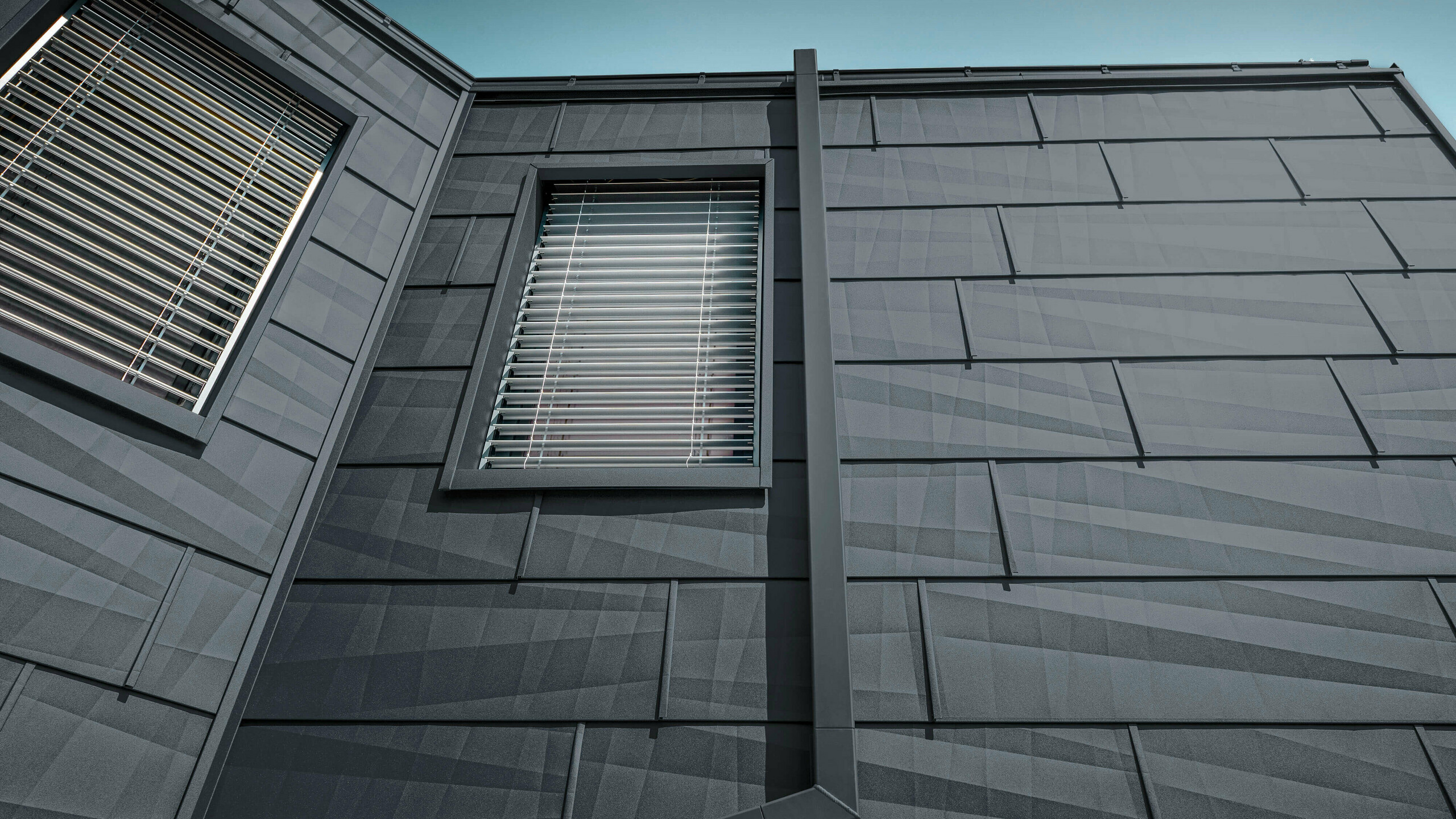 Façade clad with the PREFA FX.12 façade panel in anthracite, aluminium panels on the façade with the square downpipe, the square downpipe from PREFA in anthracite.