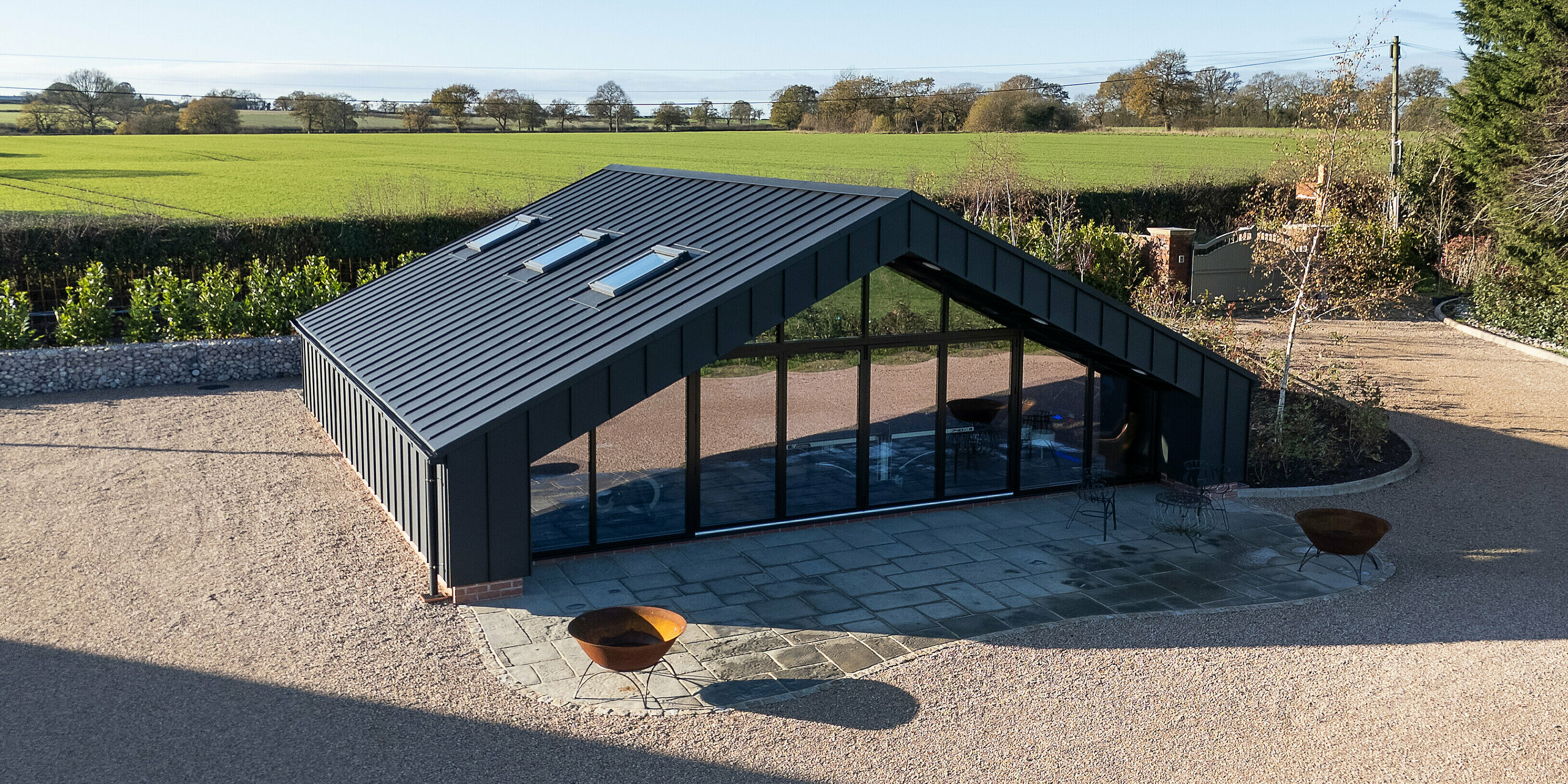 Aerial view of the modern leisure building clad entirely with PREFA aluminum and a PREFALZ standing seam roof in P.10 black. The clean roof geometry, expansive glass façade and seamless metal surface create a distinctive architectural statement. The durable, weather‑resistant aluminum envelope blends harmoniously with the surrounding open landscape.