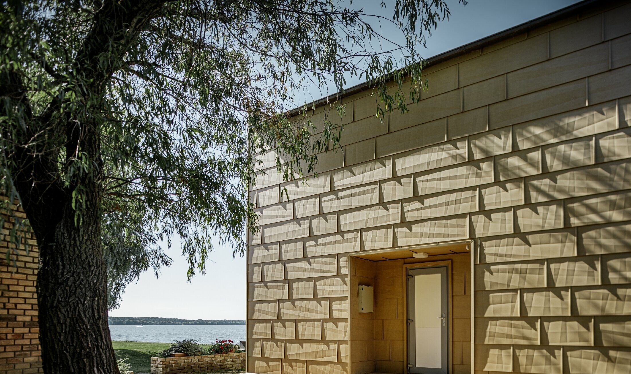 Modern lakeside weekend residence with a flat roof, large windows and a canted aluminium façade in sand brown