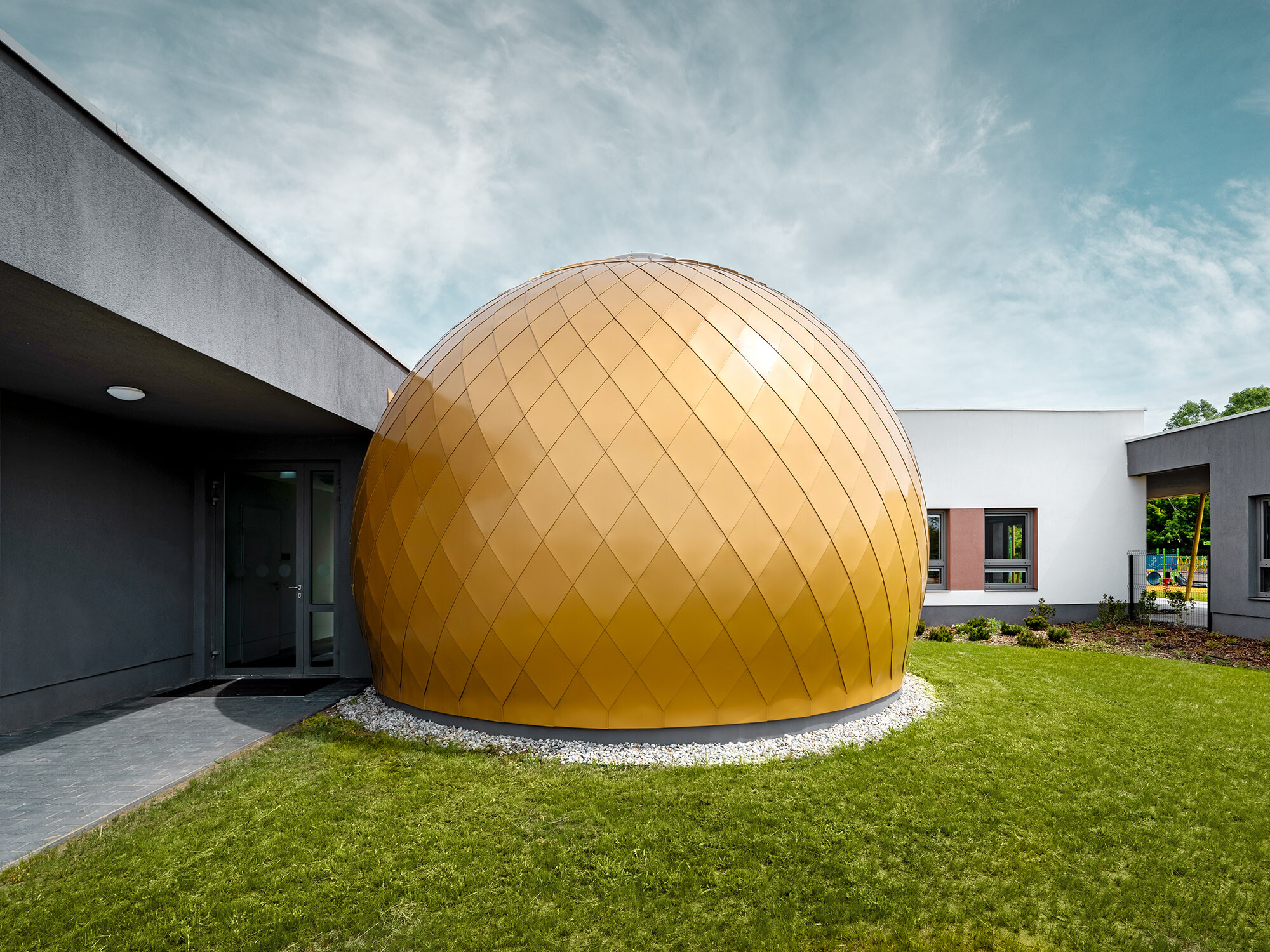 One of the three round rooms of the day nursery designed by László Erdei from the side, the plaster façade as well as the playground are partially visible next to it and behind it.