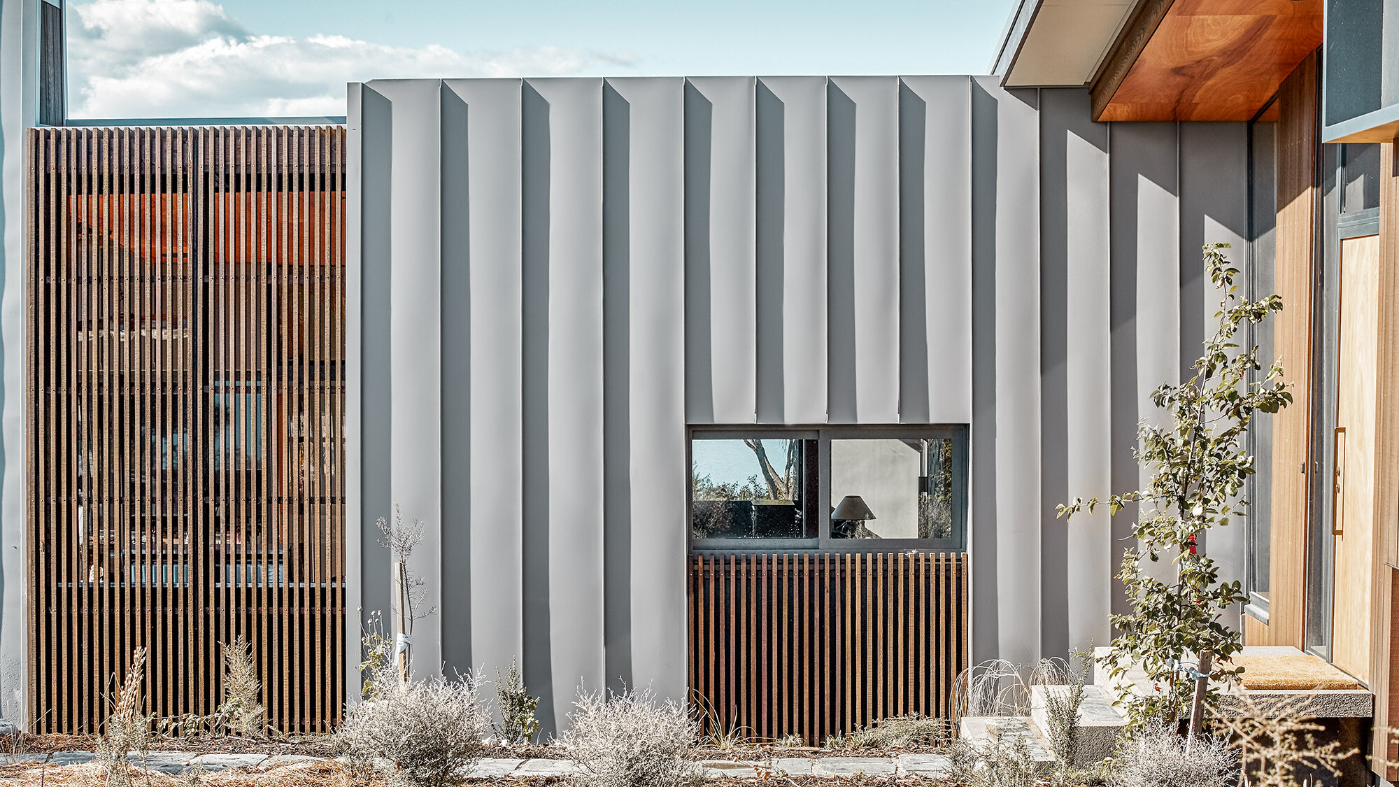 A close-up of the detached house with a focus on the timber and aluminium elements of the façade as well as part of the interior. 