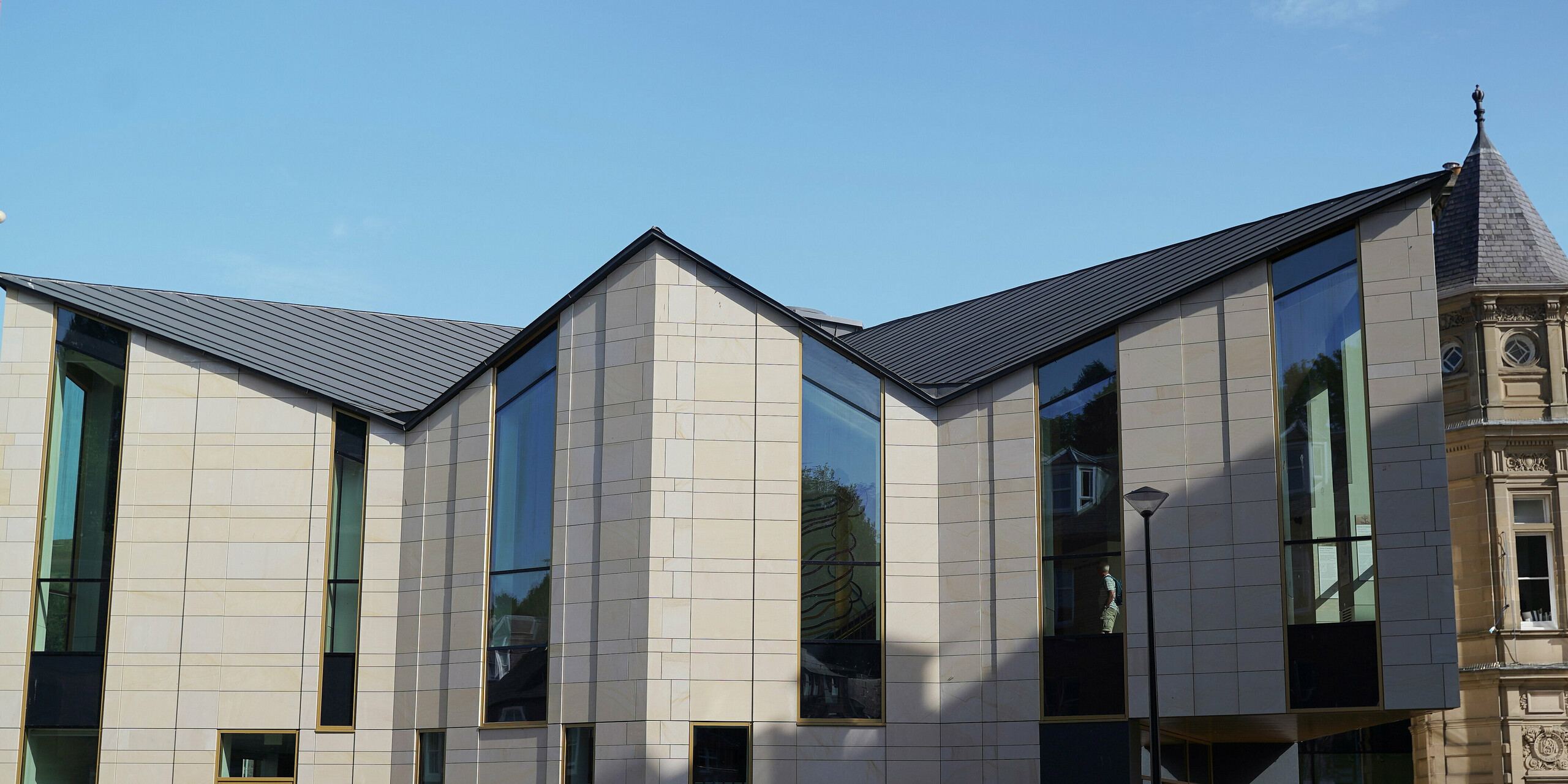 Front view of the gallery and visitor centre 'The Great Tapestry of Scotland' in Galashiels, characterised by its modern design with PREFALZ roof in P.10 zinc grey. The striking roof structure forms an architectural highlight in the historic centre of Galashiels and combines contemporary architecture with traditional buildings. The large window fronts offer a view of the cultural exhibits, while the clear roof lines emphasise the innovative orientation of the centre.