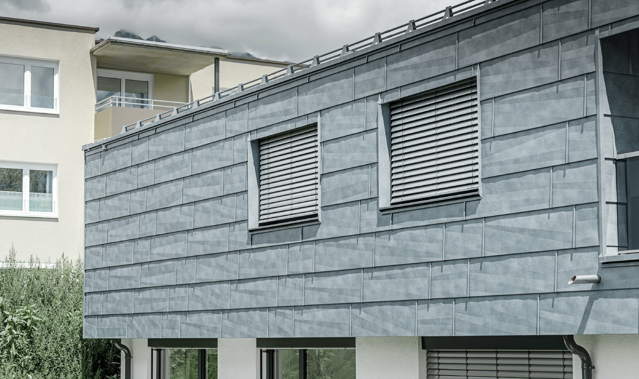 Façade surface with two windows; the façade is clad in the PREFA FX.12 façade panel in stone grey.