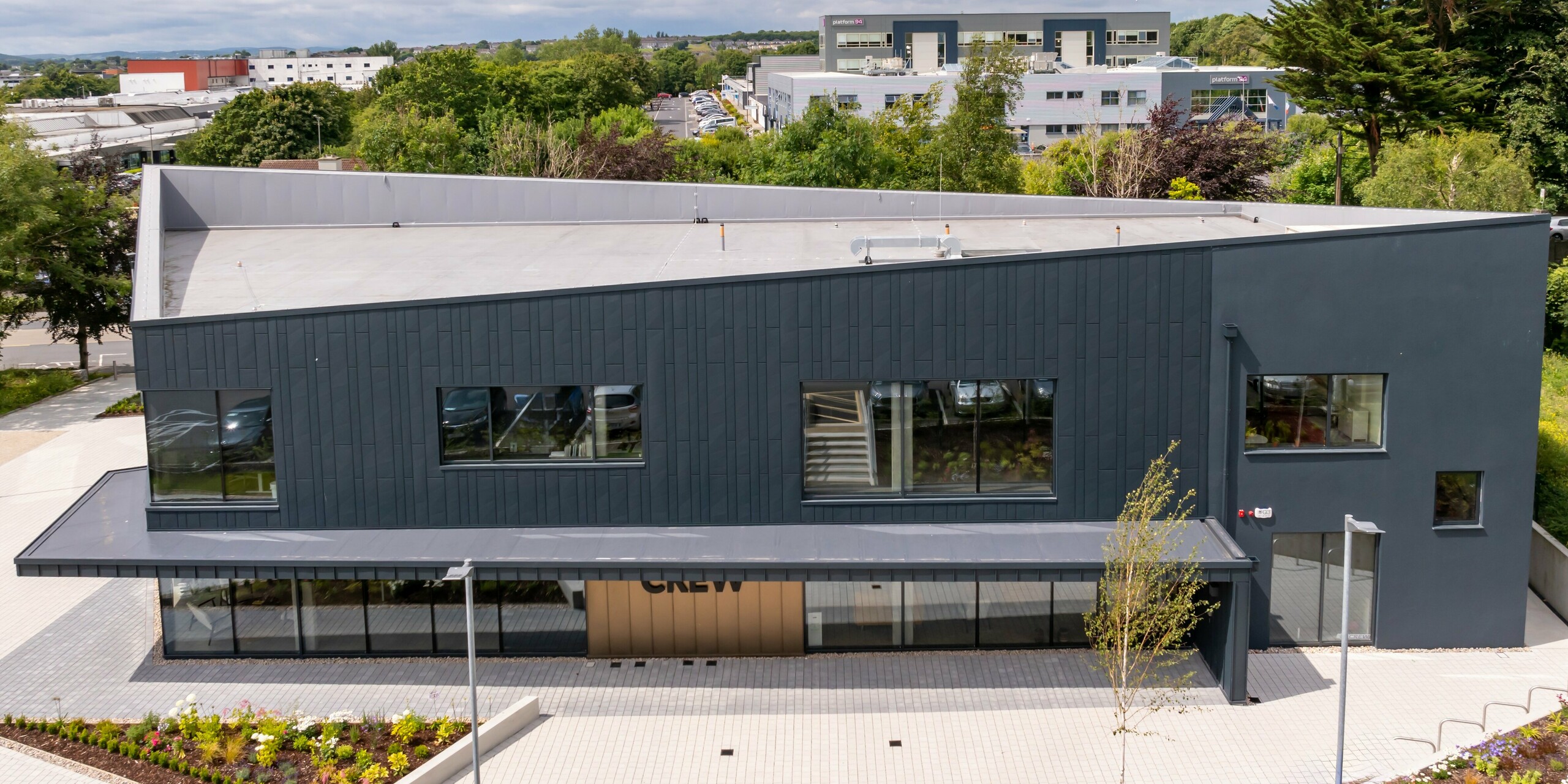 Bird's eye view of the CREW building in Galway, Ireland, with a modern façade made of PREFA Siding.X façade panels and PREFALZ in P.10 anthracite. The sloping roof lines and the clearly structured window areas emphasise the innovative design of the building. The anthracite-coloured aluminium cladding harmonises with the surroundings and gives the building a contemporary, high-quality appearance.