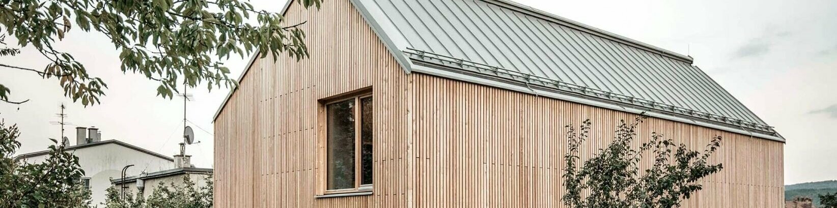 Lateral view of the detached house, which is covered in a wooden façade and clad with Prefalz in the colour zinc grey. 