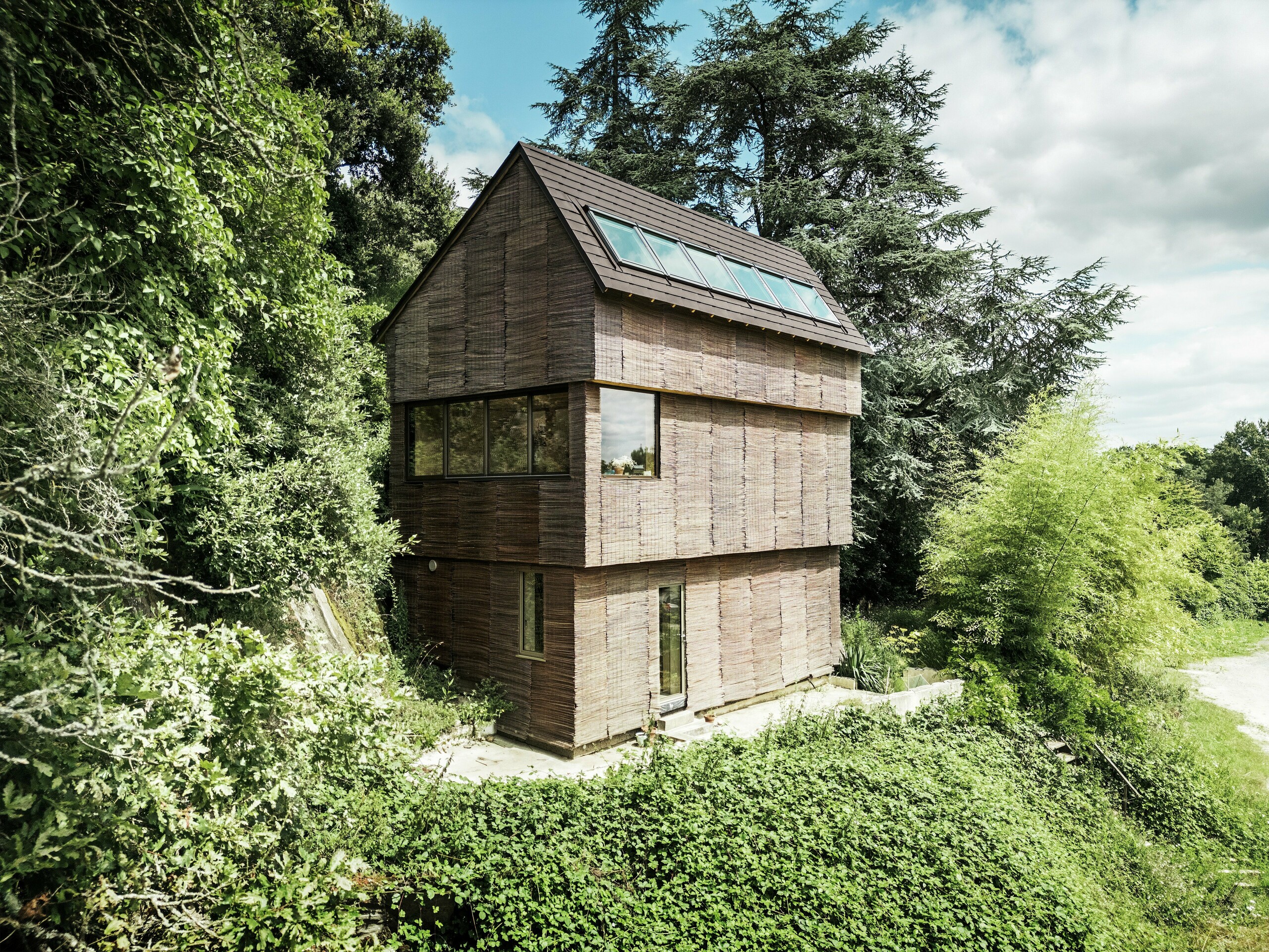 Haus in Frankreich mit PREFA Dachschindeln in P.10 Nussbraun und Weidenfassade, umgeben von natürlichem Grün – nachhaltige Architektur und umweltfreundliches Design.