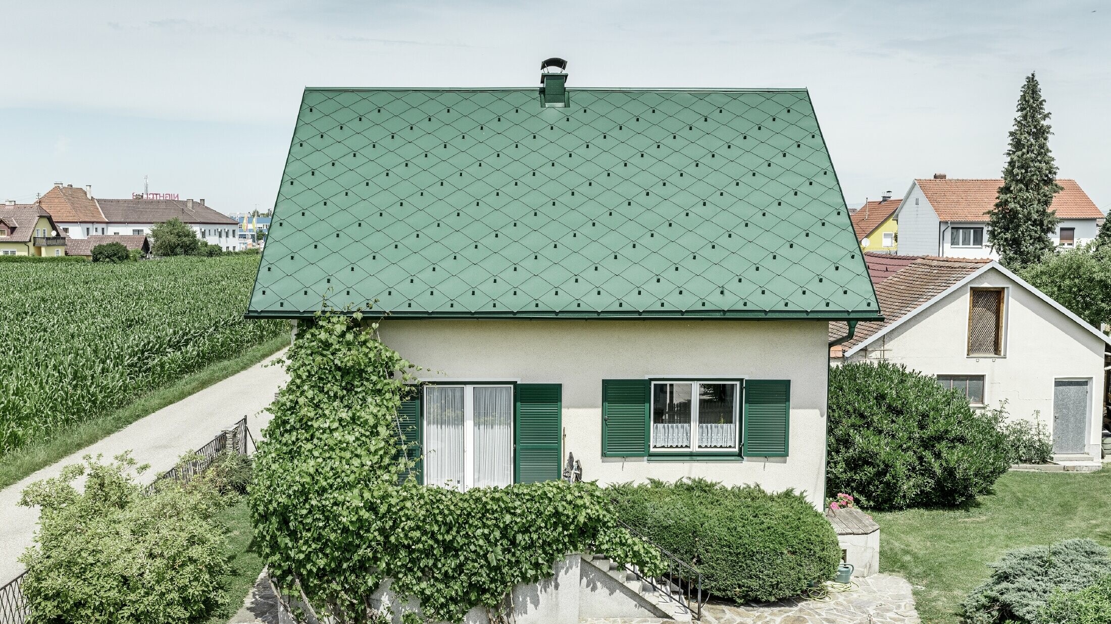 Classic detached house with a gable roof with an aluminium roof covering in moss green with green shutters. The roof was covered with PREFA rhomboid roof tiles 44 × 44 in P.10 moss green.