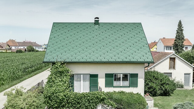 Classic detached house with a gable roof with an aluminium roof covering in moss green with green shutters. The roof was covered with PREFA rhomboid roof tiles 44 × 44 in P.10 moss green.