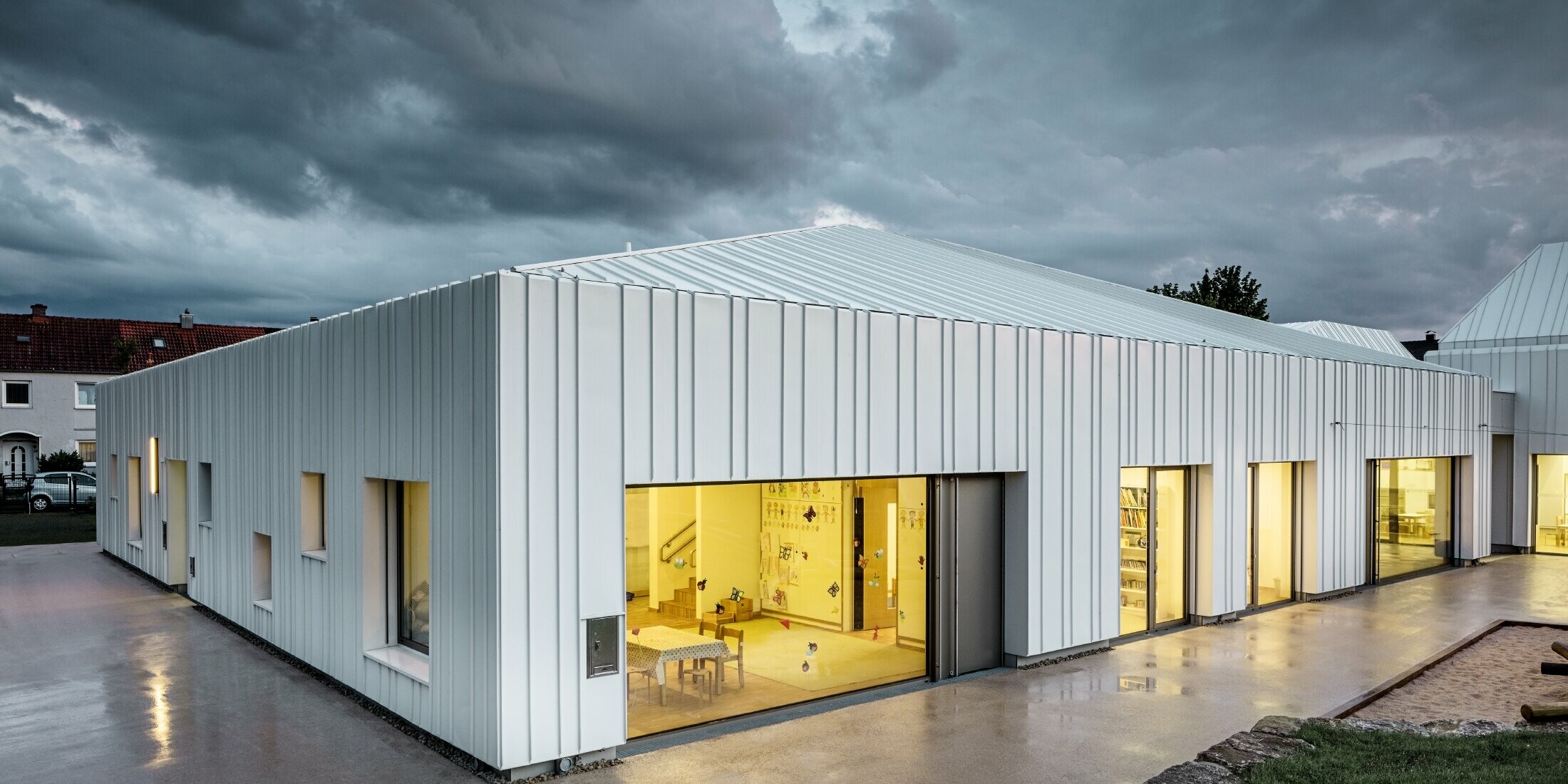 Day nursery in Niederwerrn with PREFALZ roof and façade in pure white with different widths of panels photographed at dusk and in a cloudy atmosphere