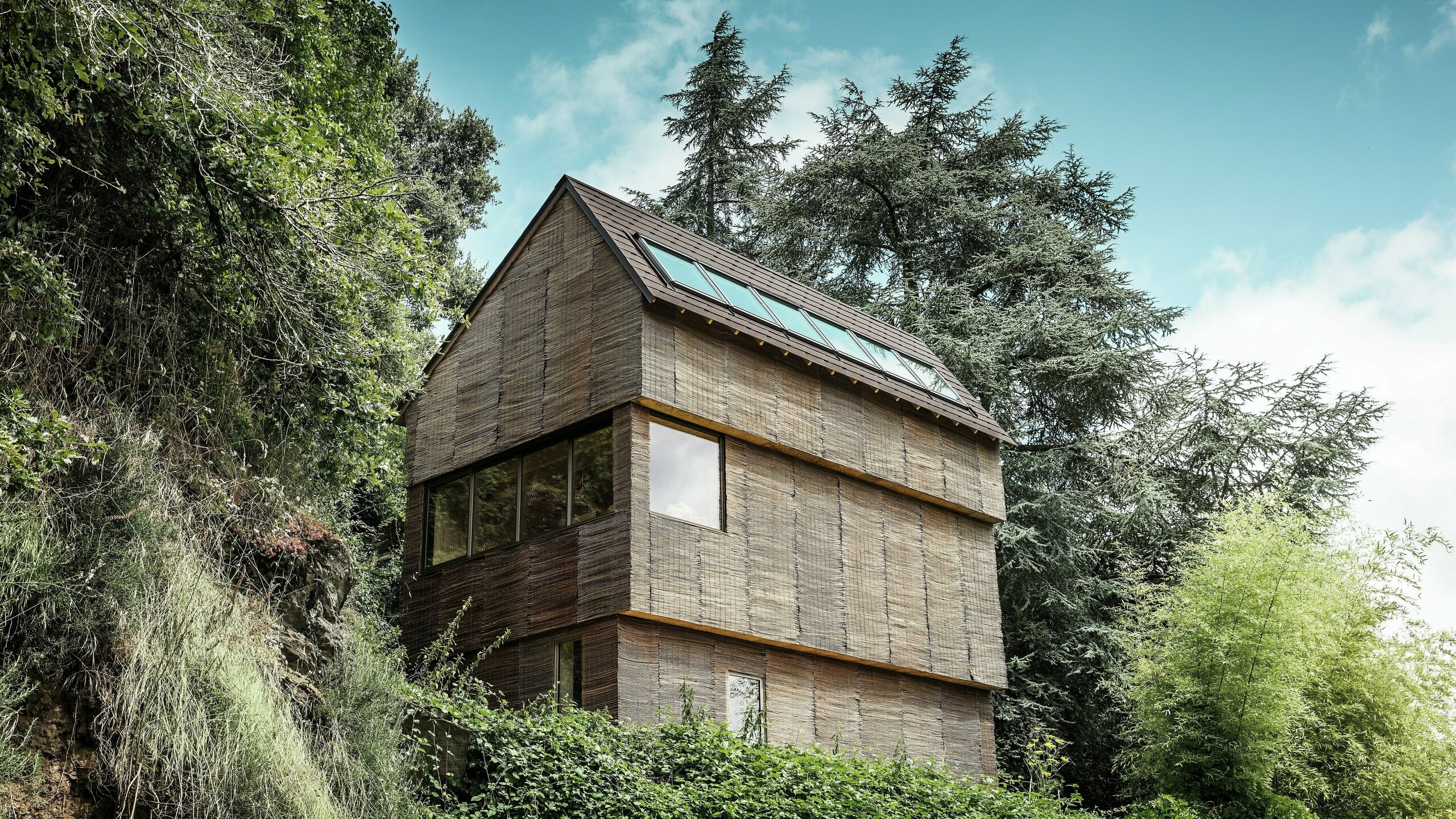 Haus im Westen Frankreichs mit PREFA Dachschindeln in P.10 Nussbraun auf steilem Hügel – modernes Design mit Weidenfassade und energieeffizientem Dach.