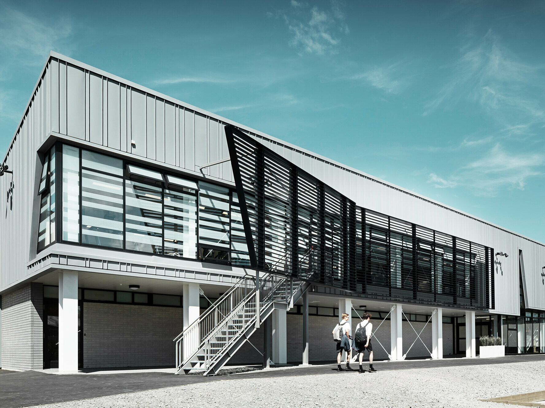 Side view of the front of the St Andrew's College Fitness Centre: Its glazing and its lined, patina grey aluminium façade are in focus, with the sky extending above.