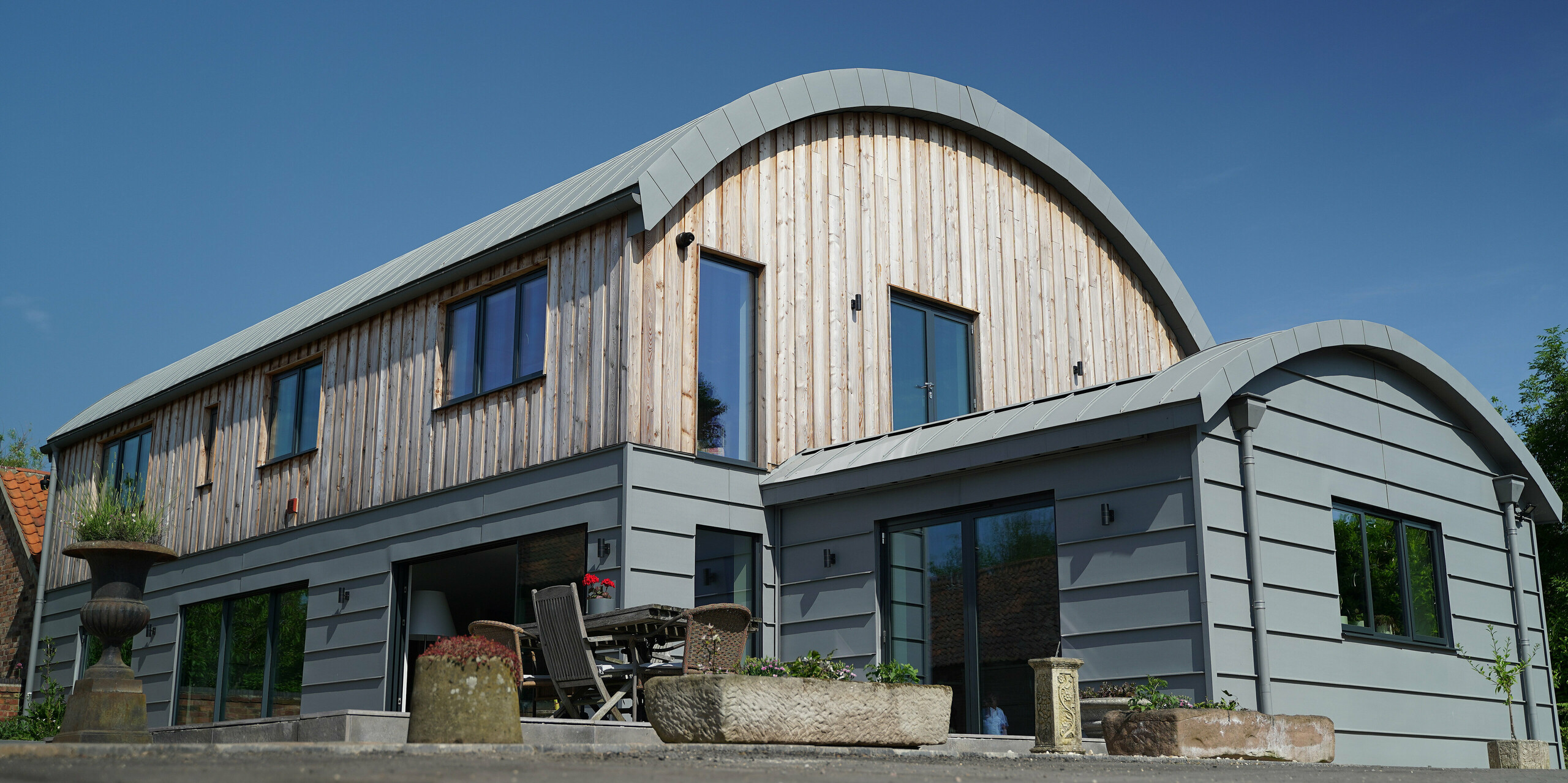 Lateral perspective on the Dutch barn clad with wood and PREFALZ in patina grey