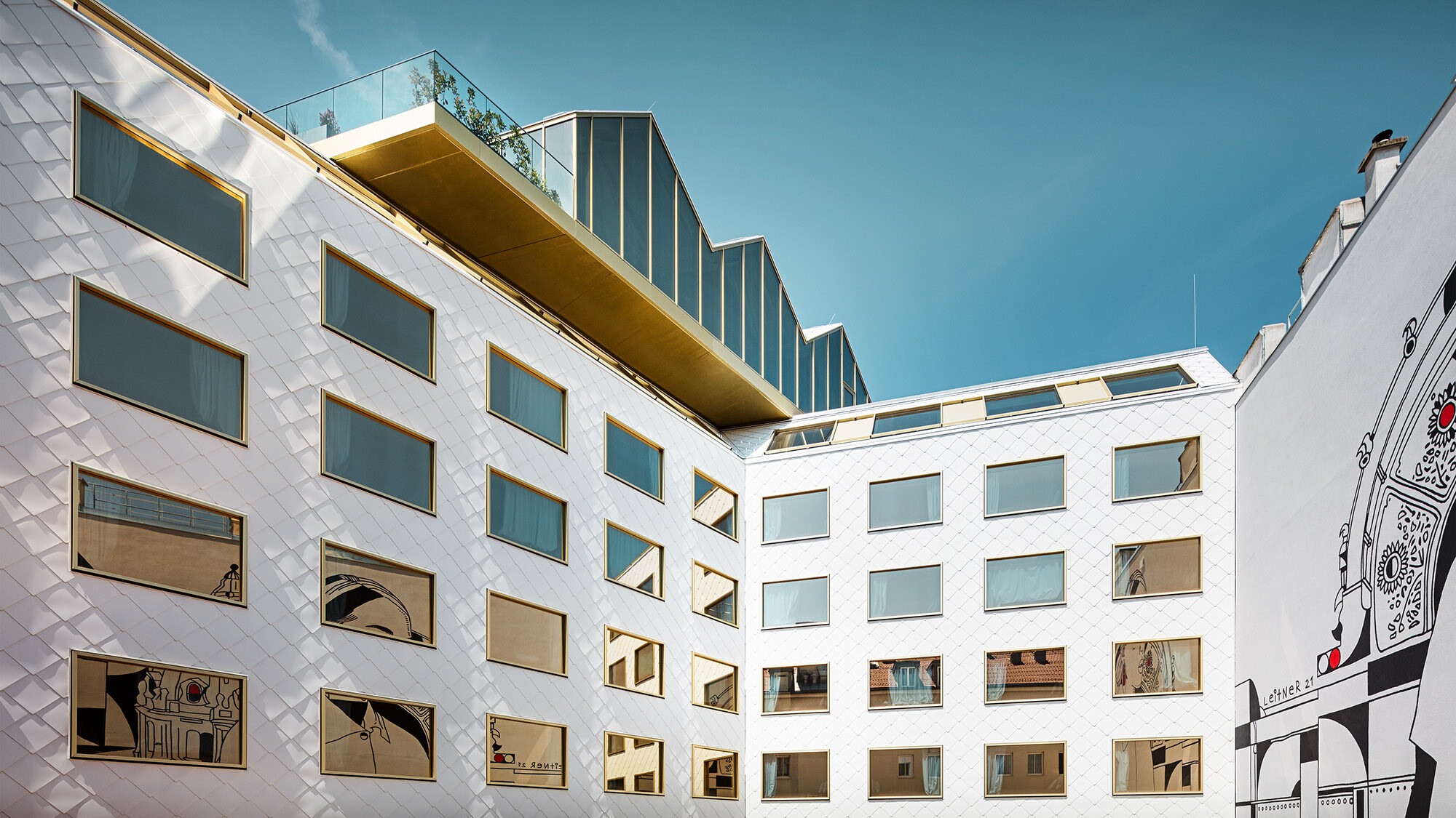 View of the hotel from the inner courtyard; a mural is reflected in the windows, the rooftop bar slightly projects over the hotel.