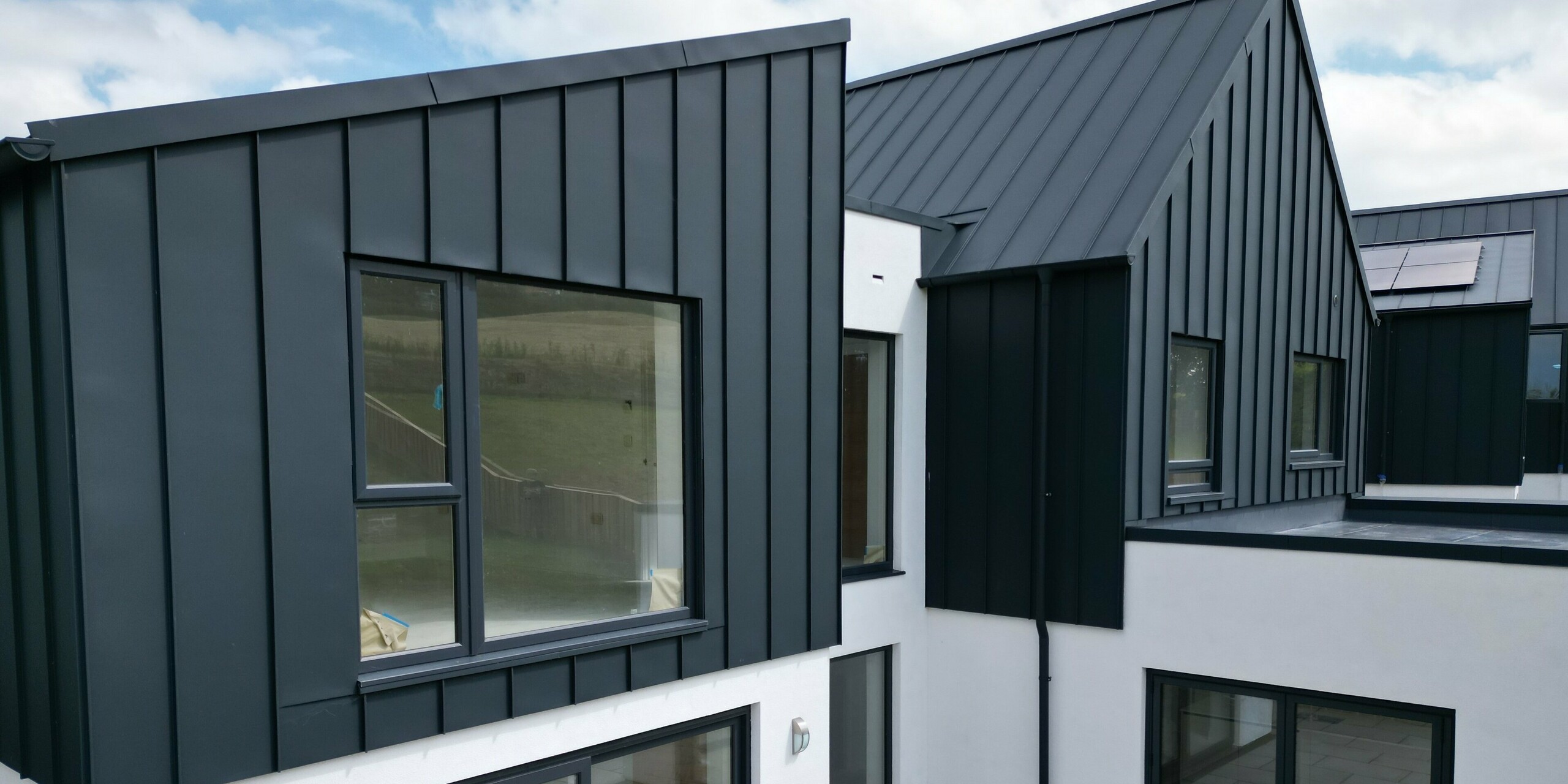 Detailed view of a single-family-house with garden and terrace, covered with PREFALZ in P.10 anthracite. The aluminium standing seam roof combines modern design with durability and underlines the sustainable approach to construction. The large window areas ensure plenty of light in the interior.