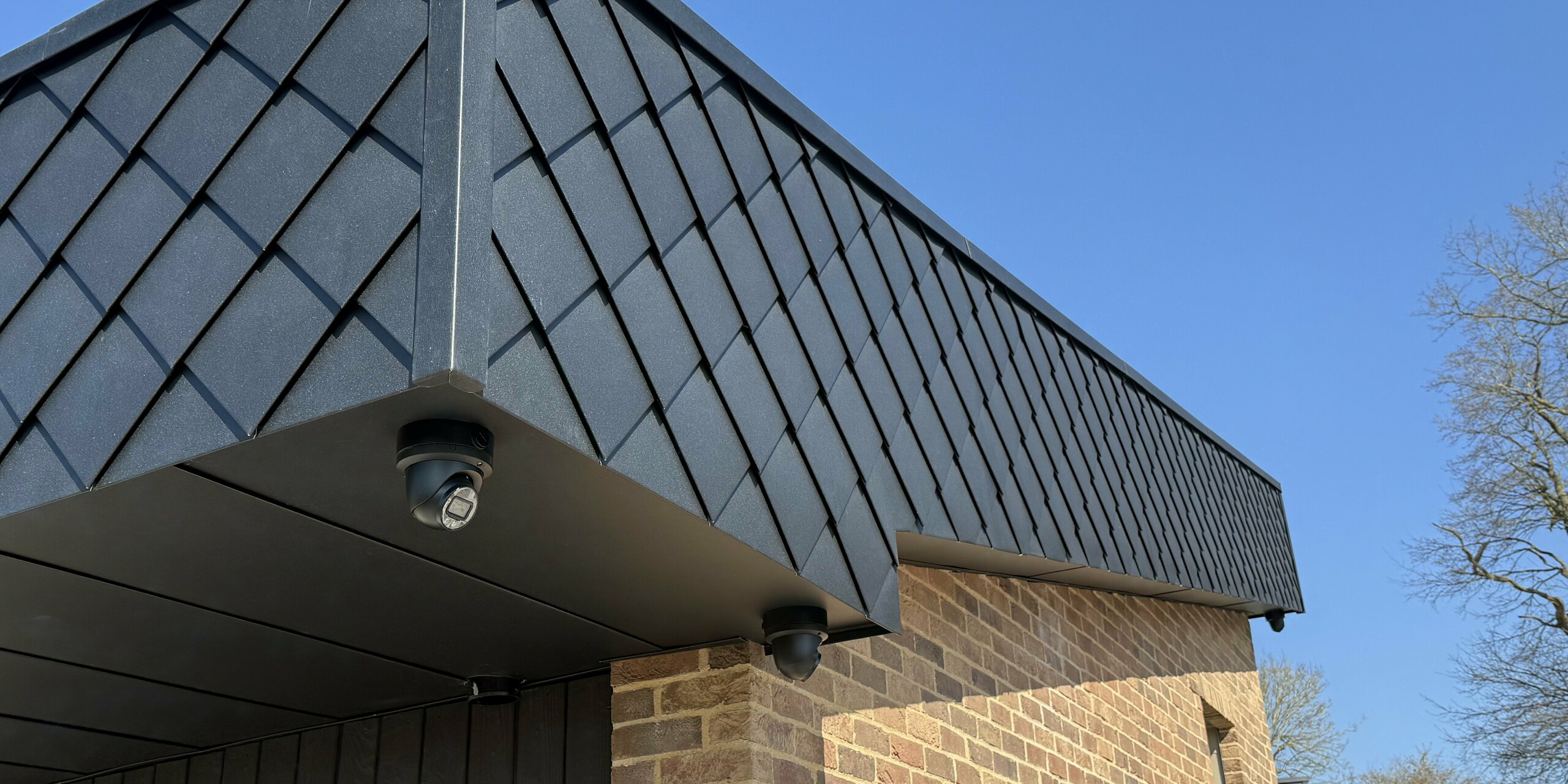 Detailansicht einer modernen Fassade des Wohnprojekts „Doone Brae Farm“ mit markantem Übergang von warmem Klinker zu eleganten PREFA Wandrauten 20 × 20 in P.10 Anthrazit. Die Aluminiumrauten bilden einen dynamischen Eyecatcher und unterstreichen die klare Linienführung des Gebäudes. Der Kontrast zwischen natürlichem Klinker und hochwertigem Aluminium schafft ein zeitloses, energieeffizientes Design.