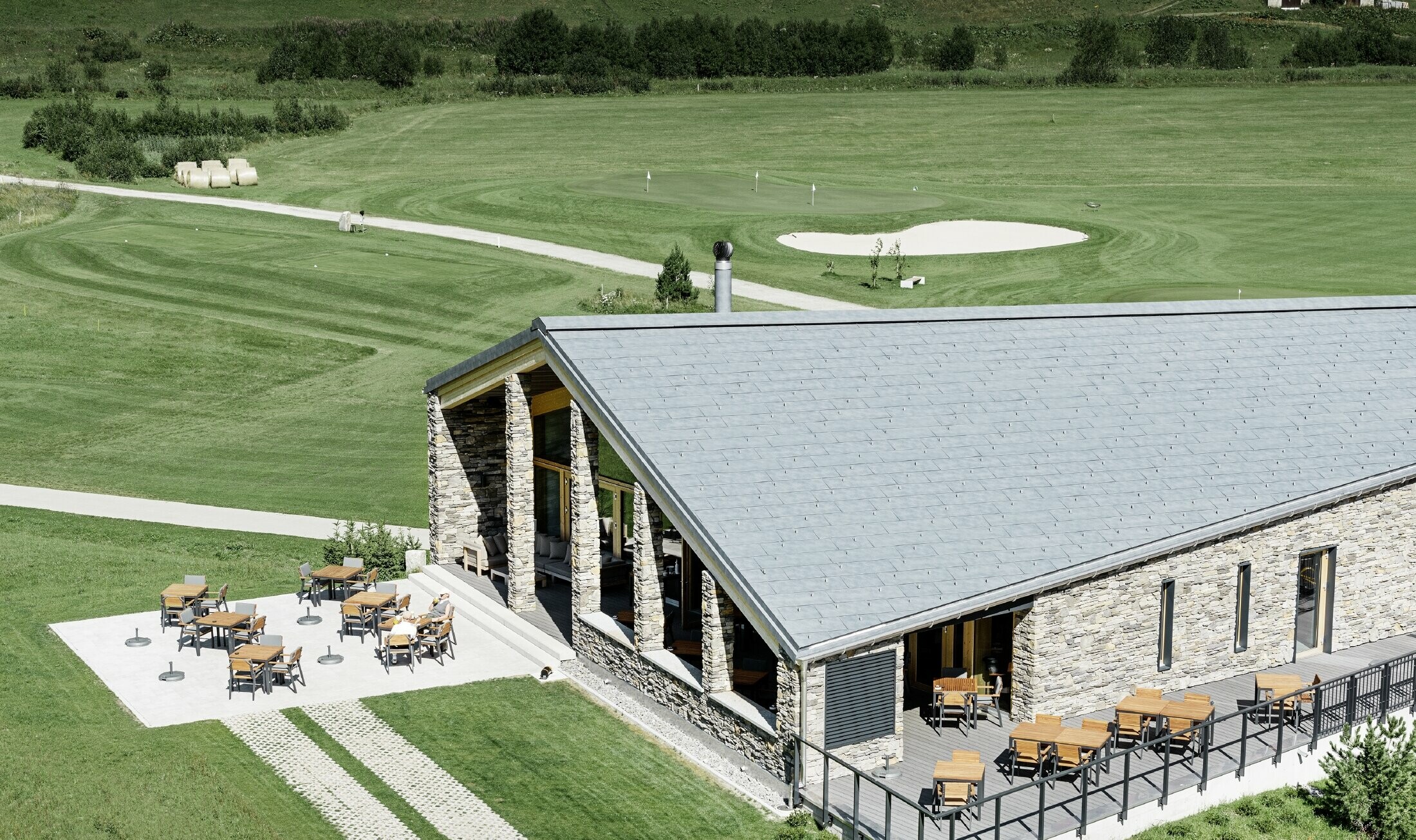 Modern club house at Andermatt golf course (Switzerland) with a stone façade and aluminium PREFA FX.12 roof panels in stone grey