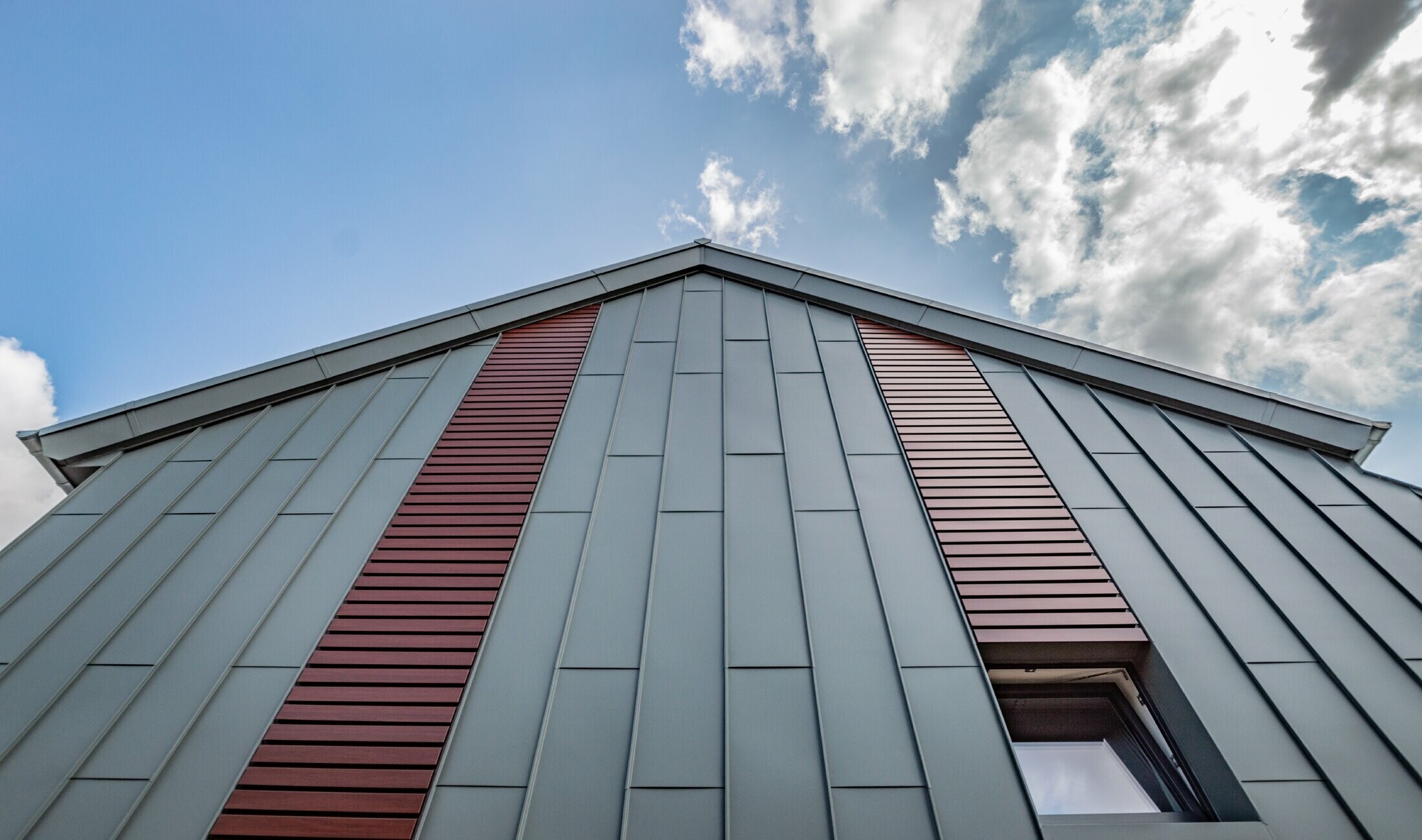 Vertical angled standing seam façade with panel covering in light grey, as well as siding horizontally in dark wood by PREFA.