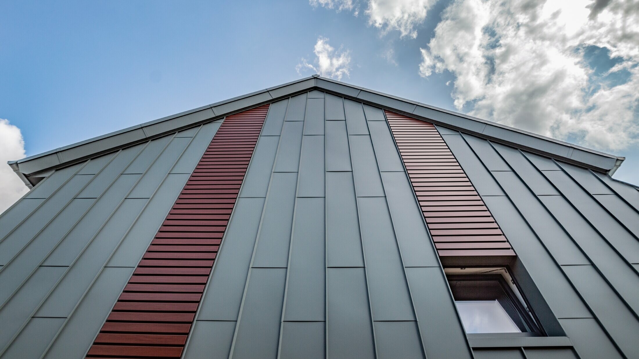 Vertical angled standing seam façade with panel covering in light grey, as well as siding horizontally in dark wood by PREFA.