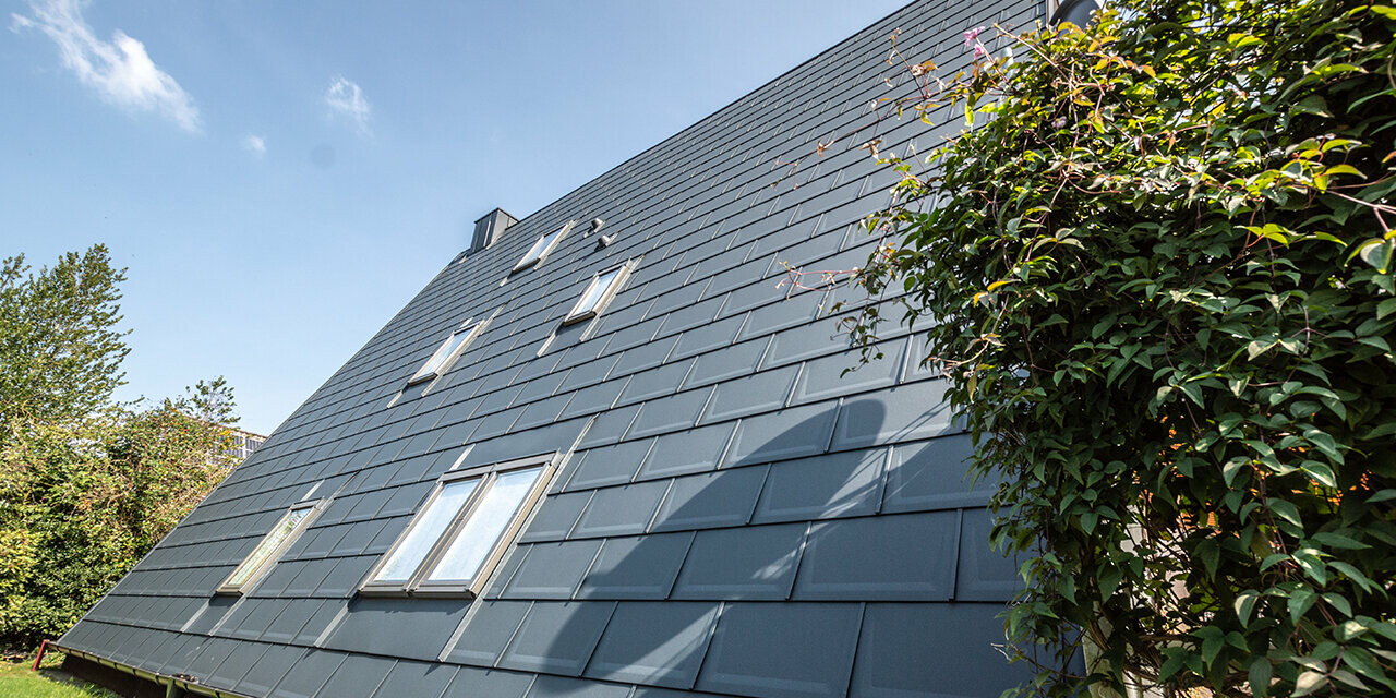 The long roof area of an A-frame house covered with the PREFA roof tile in P.10 anthracite. A number of roof-top windows are integrated into the roof area.