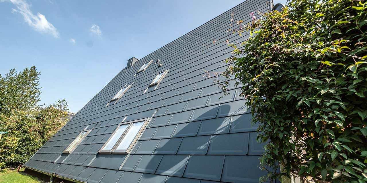 The long roof area of an A-frame house covered with the PREFA roof tile in P.10 anthracite. A number of roof-top windows are integrated into the roof area.