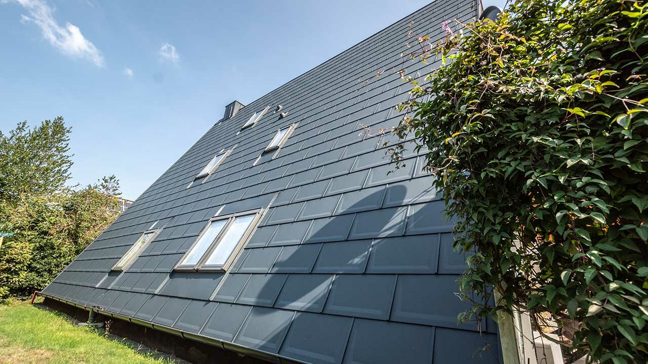 The long roof area of an A-frame house covered with the PREFA roof tile in P.10 anthracite. A number of roof-top windows are integrated into the roof area.