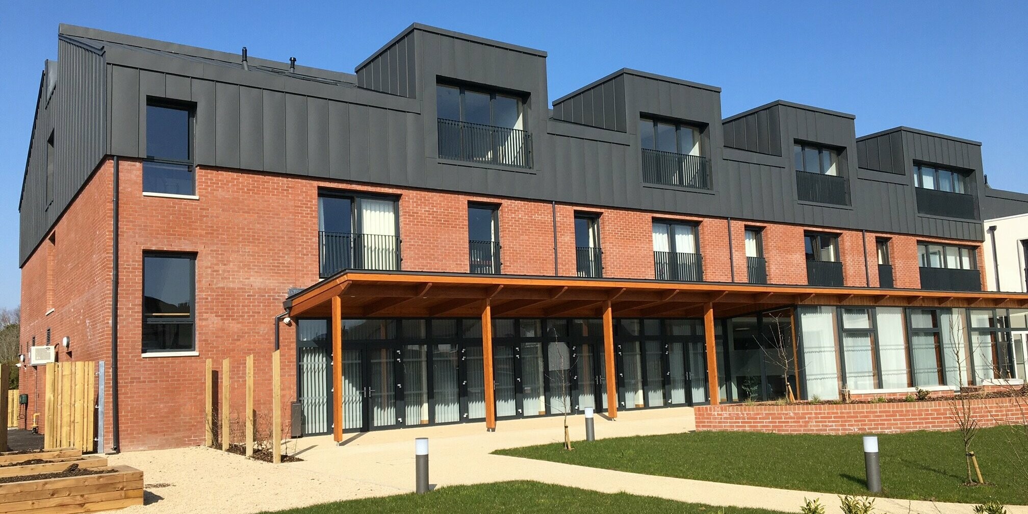 Rear view of Harberton Hall in Belfast with spacious garden area. The PREFALZ aluminium cladding in P.10 dark grey and the classic brick walls create a stylish overall look. The innovative standing seam technology emphasises the functionality and aesthetics of the roof landscape with several flat roof dormers.