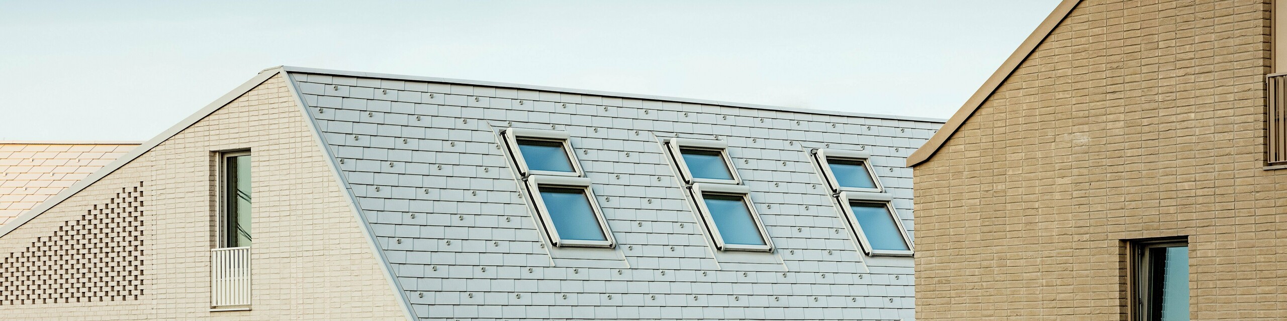 Markante Dachlandschaft im neuen Stadtquartier Vydrica in Bratislava: Steil geneigte Dächer mit präzise verlegten PREFA Aluminium Dachschindeln in P.10 Prefaweiß setzen mit ihren klaren Linien und rhythmisch angeordneten Dachfenstern eindrucksvolle Akzente. Die homogene Oberfläche verbindet Dach und Fassade zu einer eleganten Einheit und greift die ruhige Formsprache der Altstadt auf. PREFA Aluminium überzeugt dabei durch geringes Gewicht, hohe Stabilität, extreme Witterungsbeständigkeit und langlebige, wartungsarme Qualität – ideal für komplexe, architektonisch anspruchsvolle Dachlösungen.