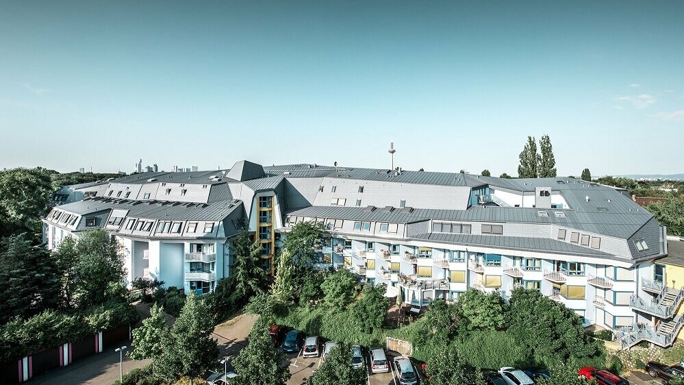 renovated roofscape, entire house in the background the Frankfurt skyline, multi-storey residential and nursing home, aluminium roof made of Prefalz and PREFA shingles, design language organic architecture