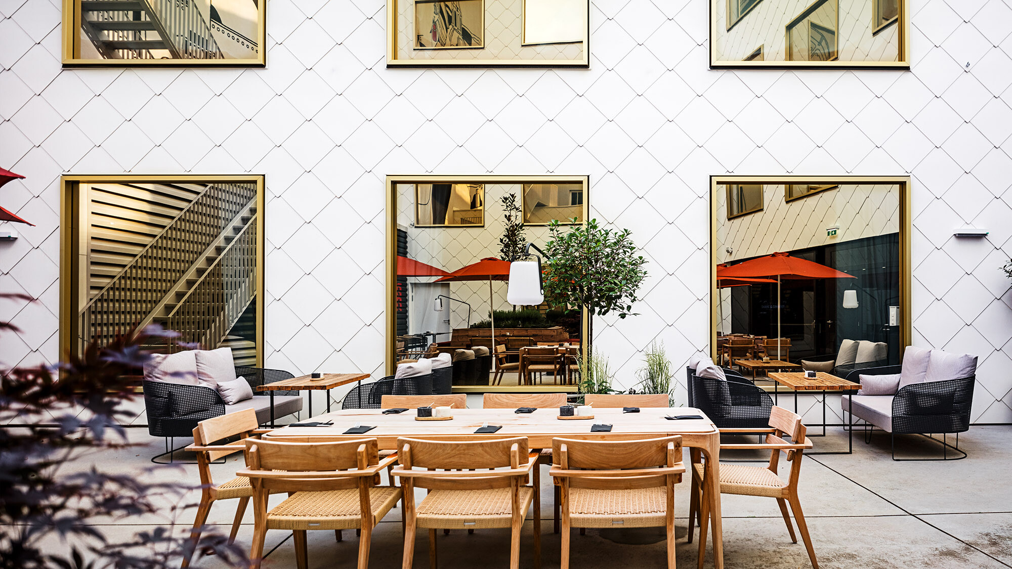 The outside seating areas belonging to the hotel, the white rhomboid tile façade with its mirror-glazed windows can be seen in the background.