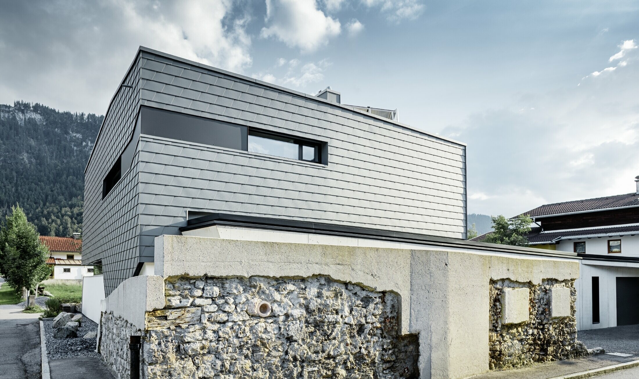 Modern detached house with a flat roof, large windows and a shingle façade in light grey, made of aluminium by PREFA