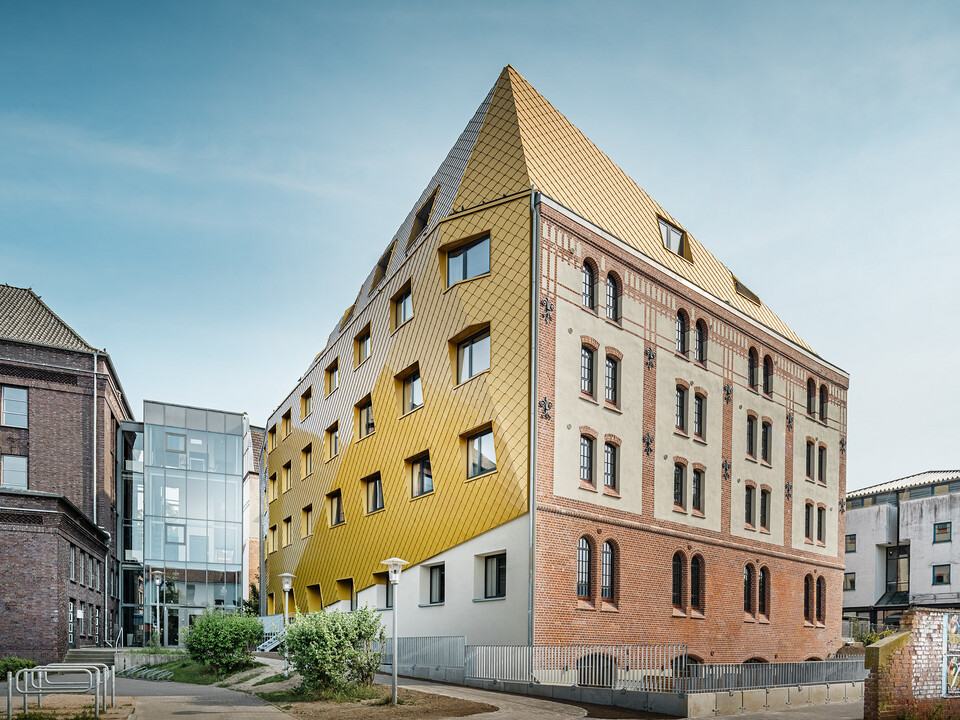 The student residence from a worm's eye view: the historic façade extending on the right, the new PREFA envelope wrapping itself along the building and up over the attic on the left side. 